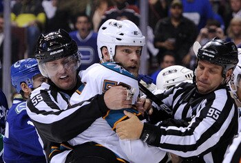 VANCOUVER, BC - MAY 18:  NHL Linesmen Shane Heyer #55 and Jonny Murray #95 hold back Ben Eager #55 of the San Jose Sharks as Eager gets called for an unsportsmanlike conduct penalty for standing over goaltender Roberto Luongo #1 of the Vancouver Canucks a