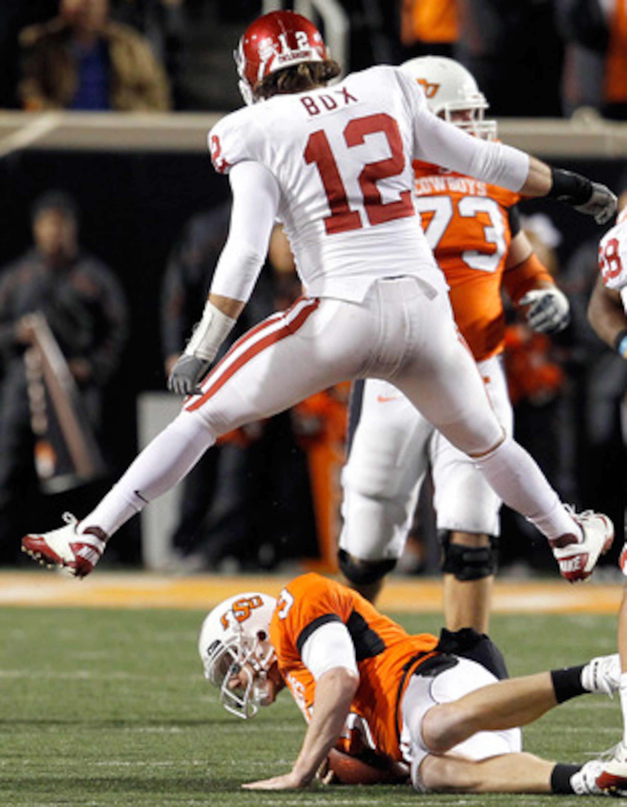 STILLWATER, OK - NOVEMBER 27:  Linebacker Austin Box #12 of the Oklahoma Sooners leaps over quarterback Brandon Weeden #3 of the Oklahoma State Cowboys after Weeden was sacked for a loss at Boone Pickens Stadium on November 27, 2010 in Stillwater, Oklahom