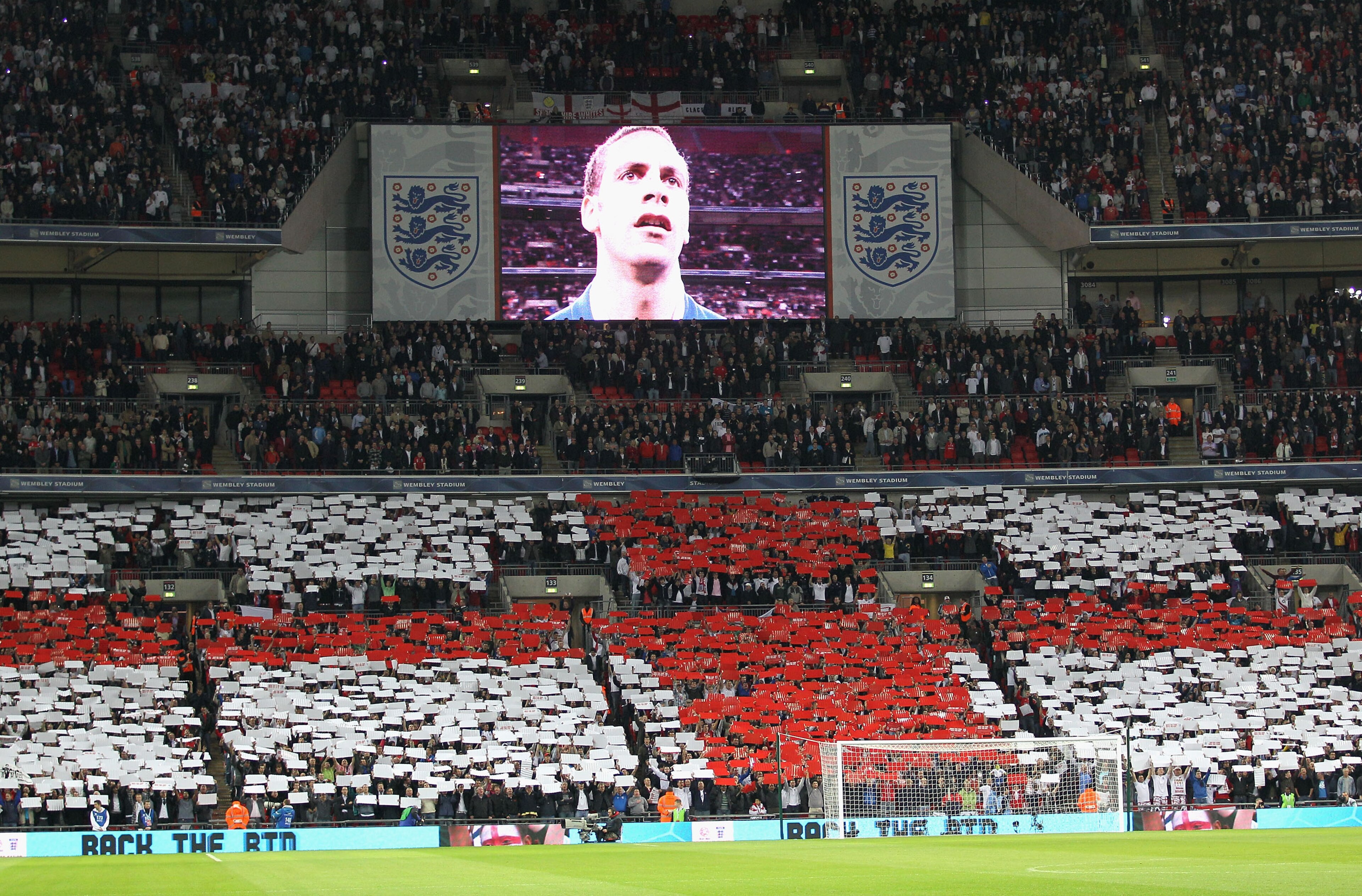 LONDON, ENGLAND - OCTOBER 12: Captain Rio Ferdinand of England is seen on the TV screen as England fans show their support during the national anthem during the UEFA EURO 2012 Group G Qualifying match between England and Montenegro at Wembley Stadium on O