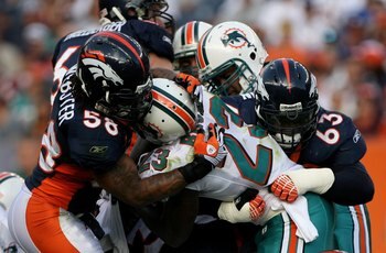DENVER - NOVEMBER 02:  Running back Ronnie Brown #23 of the Miami Dolphins is stopped by defensive tackle Dewayne Robertson #63 and linebacker Nate Webster #58 of the Denver Broncos during NFL action at Invesco Field at Mile High on November 2, 2008 in De