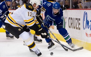 VANCOUVER, CANADA - FEBRUARY 26: Mason Raymond #21 of the Vancouver Canucks tries to chip the puck past Tomas Kaberle #12 of the Boston Bruins during the second period in NHL action on February 26, 2011 at Rogers Arena in Vancouver, British Columbia, Cana