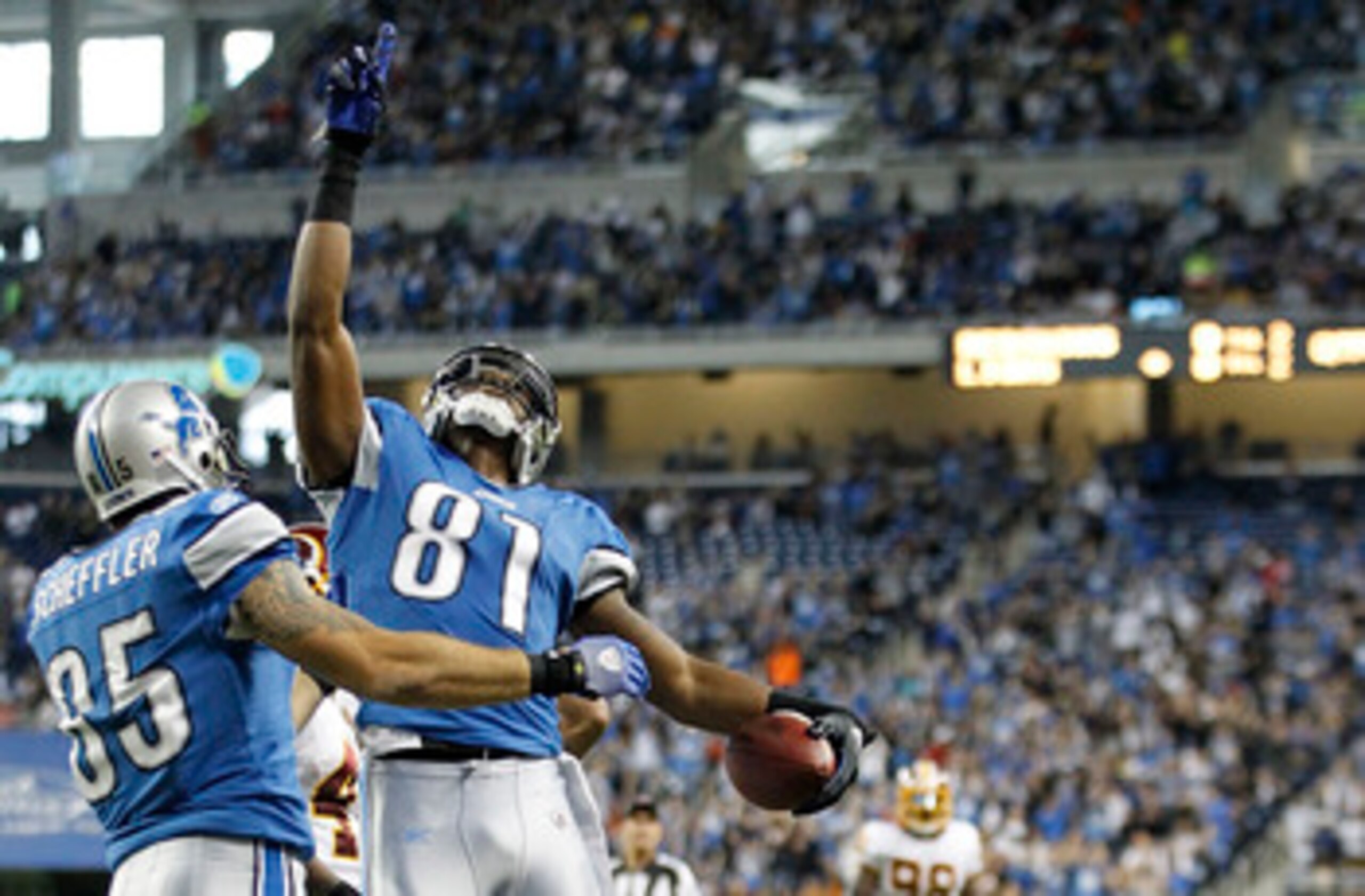 DETROIT - OCTOBER 31:  Calvin Johnson #81 of the Detroit Lions scores a second quarter touchdown as is congratuated by teamate Tony Scheffler #85 as Lorenzo Alexander #97 of the Washington Redskins looks on during the game at Ford Field on October 31, 201