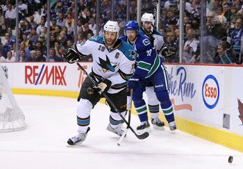 VANCOUVER, CANADA - MAY 24:  Joe Thornton #19 of the San Jose Sharks looks to play the puck out of the defensive zone against the San Jose Sharks Henrik Sedin #33 of the Vancouver Canucks hooks Thornto's stick in Game Five of the Western Conference Finals