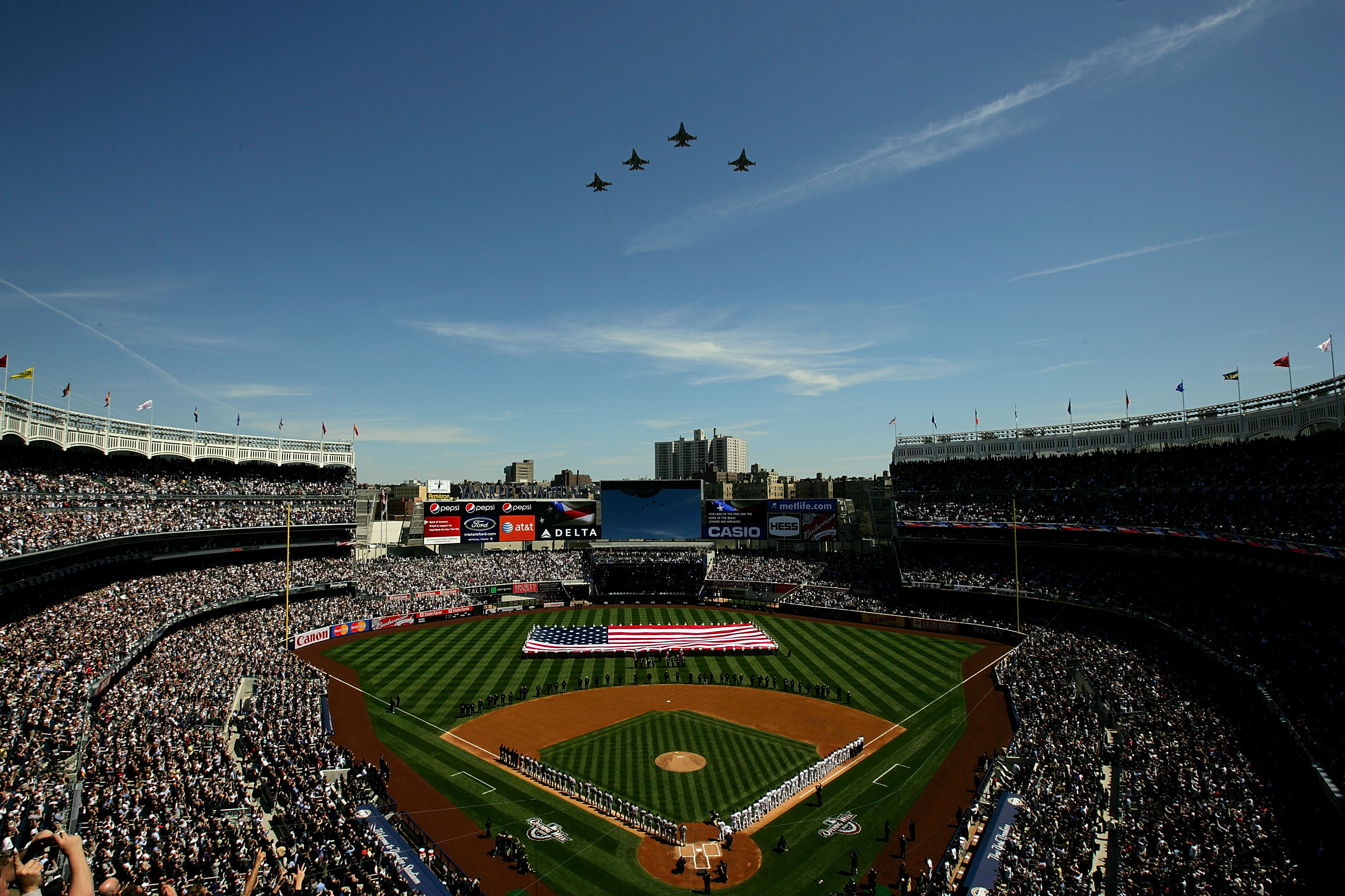 NEW YORK - APRIL 16:  Fighter jets fly over as recording artist Kelly Clarkson sings the National Anthem while members of the military hold a giant American flag before the opening day game between the Cleveland Indians and the New York Yankees at the new