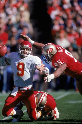 SAN FRANCISCO - NOVEMBER 17:  Quarterback Bill Kenney #9 of the Kansas City Chiefs gets sacked by defensive end Fred Dean and Michael Carter #95 of the San Francisco 49ers during a game at Candlestick Park on November 17, 1985 in San Francisco, California