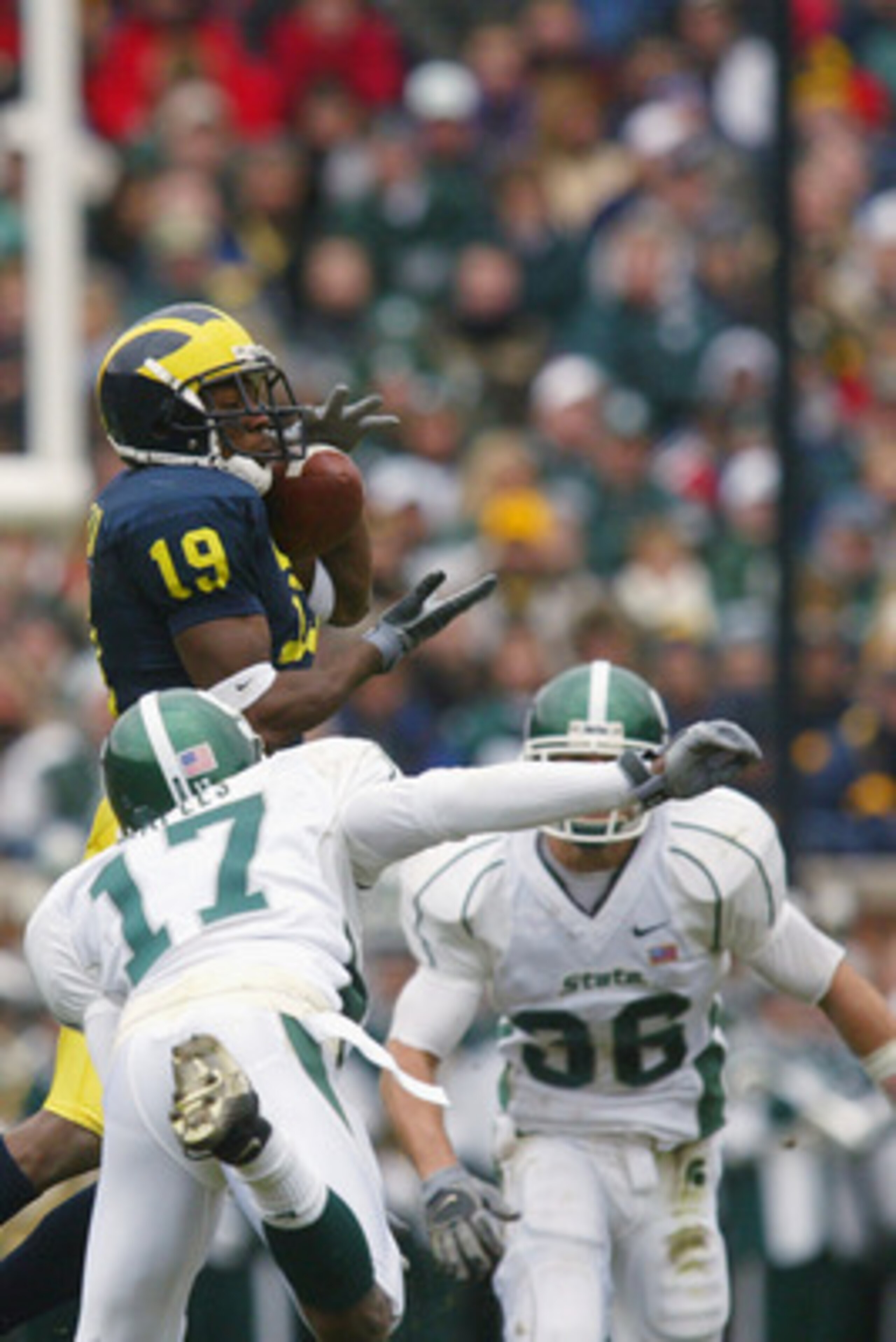 ANN ARBOR, MI - NOVEMBER 2: Ronald Bellamy #19 of the Michigan Wolverines catches the ball over Roderick Maples #17 and Eric Smith #36 of the Michigan State Spartans on November 2, 2002 at Michigan Stadium in Ann Arbor, Michigan. Michigan defeated Michi ANN ARBOR, MI - NOVEMBER 2: Ronald Bellamy #19 of the Michigan Wolverines catches the ball over Roderick Maples #17 and Eric Smith #36 of the Michigan State Spartans on November 2, 2002 at Michigan Stadium in Ann Arbor, Michigan. Michigan defeated Michi