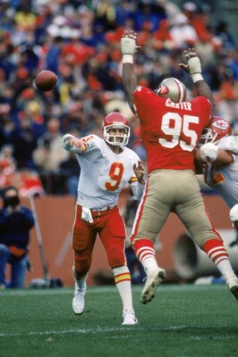 SAN FRANCISCO - NOVEMBER 17:  Quarterback Bill Kenney #9 of the Kansas City Chiefs attempts to pass over defensive linemen Michael Carter #95 of the San Francisco 49ers during a game at Candlestick Park on November 17, 1985 in San Francisco, California.  