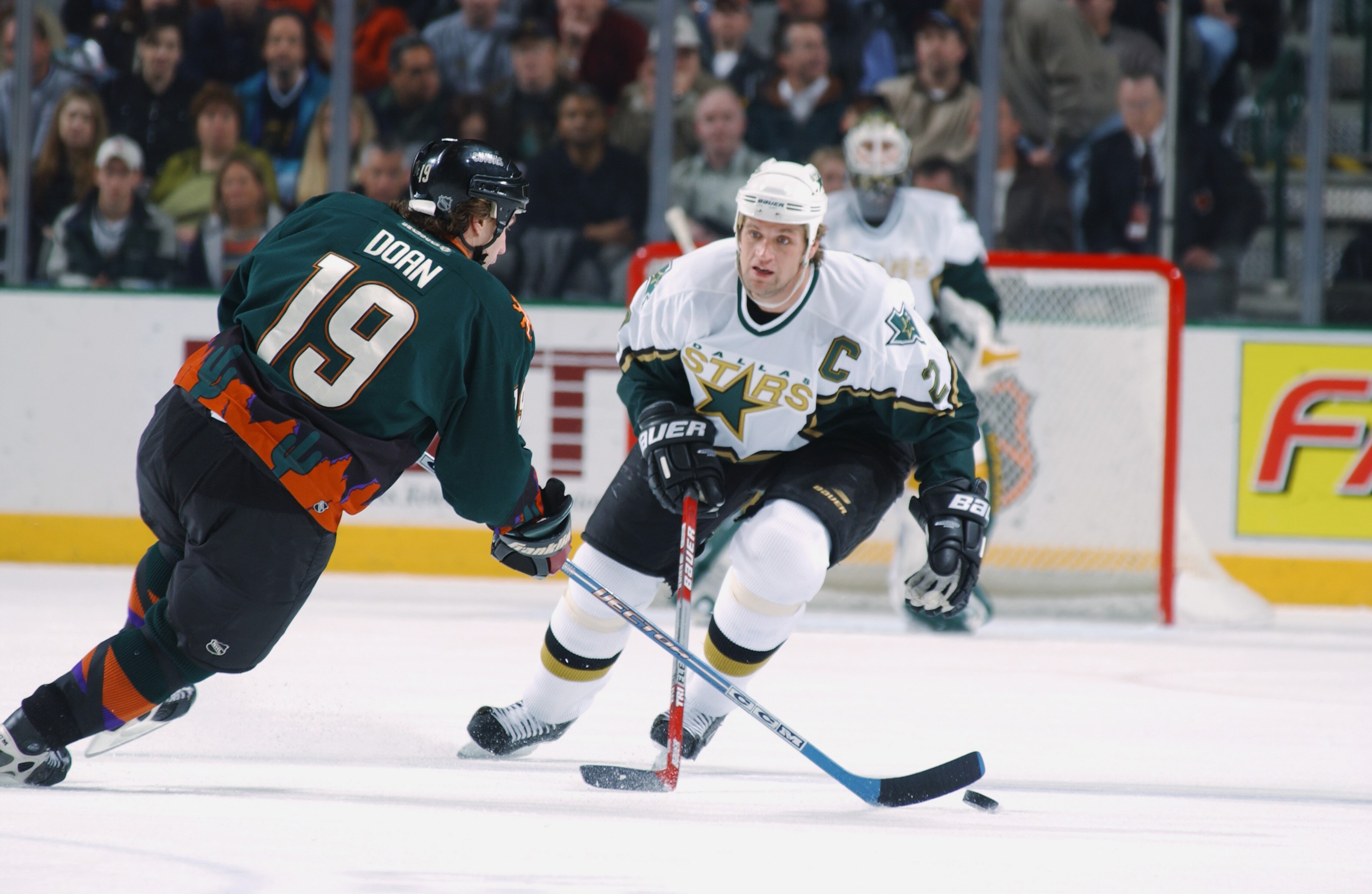DALLAS - FEBRUARY 21:  Shane Doan #19 of the Phoenix Coyotes tries to carry the puck past Derian Hatcher #2 of the Dallas Stars during the game at the American Airlines Center on February 21, 2003 in Dallas, Texas. The Coyotes and the Stars skated to a 2-