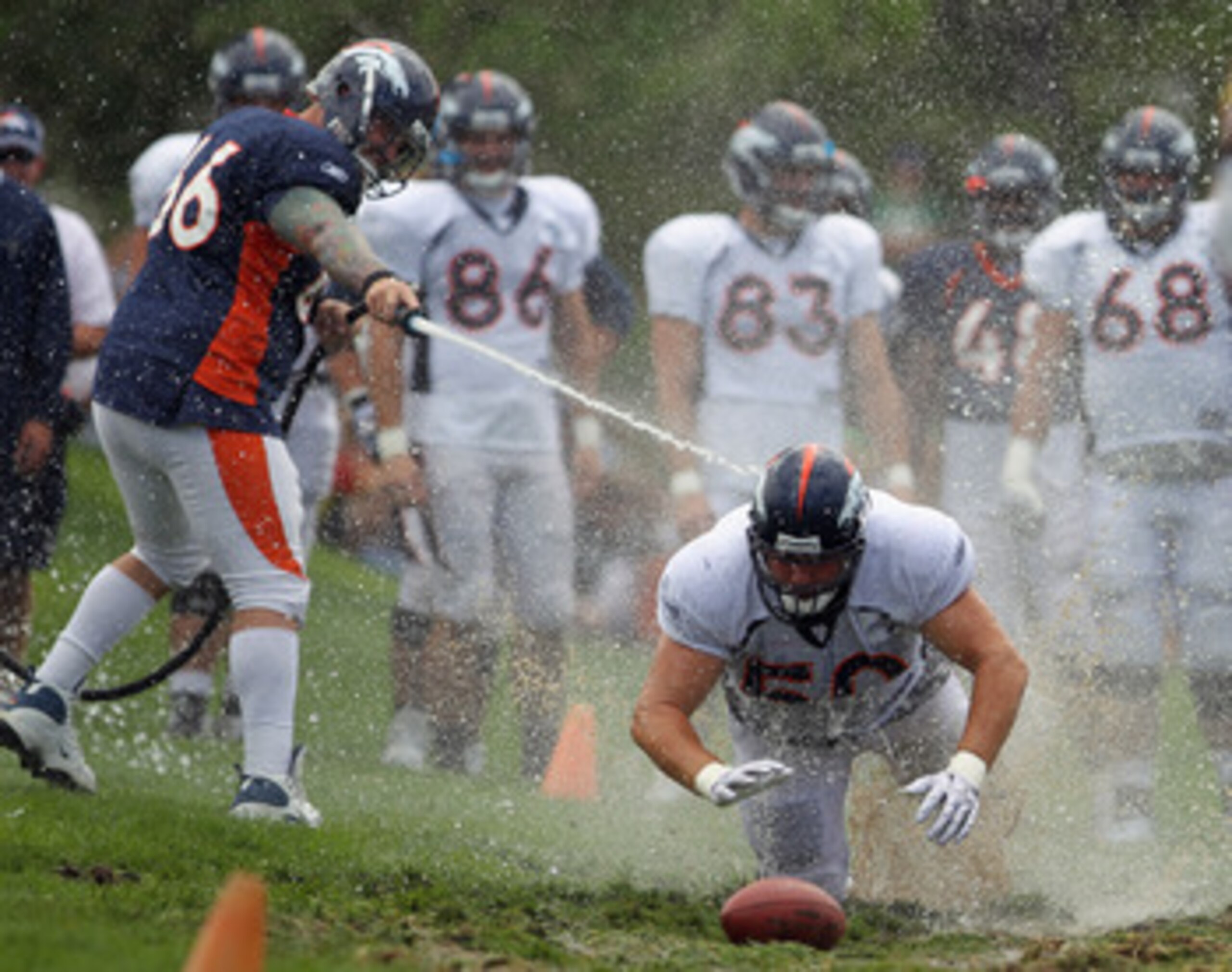 ENGLEWOOD, CO - AUGUST 05: Lonie Paxton #66 hoses down offensive lineman J.D. Walton #50 of the Denver Broncos as dives into the mud as rookies partake in the slip and slide fumble drill during training camp at Dove Valley on August 5, 2010 in Englewood, ENGLEWOOD, CO - AUGUST 05: Lonie Paxton #66 hoses down offensive lineman J.D. Walton #50 of the Denver Broncos as dives into the mud as rookies partake in the slip and slide fumble drill during training camp at Dove Valley on August 5, 2010 in Englewood,