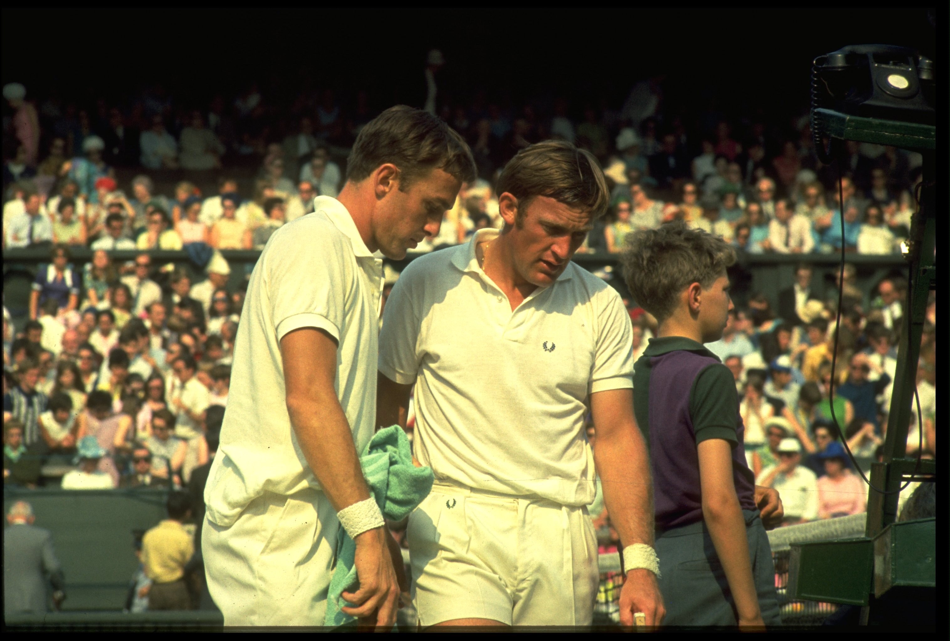 1970's:  JOHN NEWCOMBE (LEFT) AND TONY ROCHE OF AUSTRALIA DISCUSS TACTICS DURING A BREAK IN A DOUBLES MATCH AT THE WIMBLEDON TENNIS CHAMPIONSHIPS.
