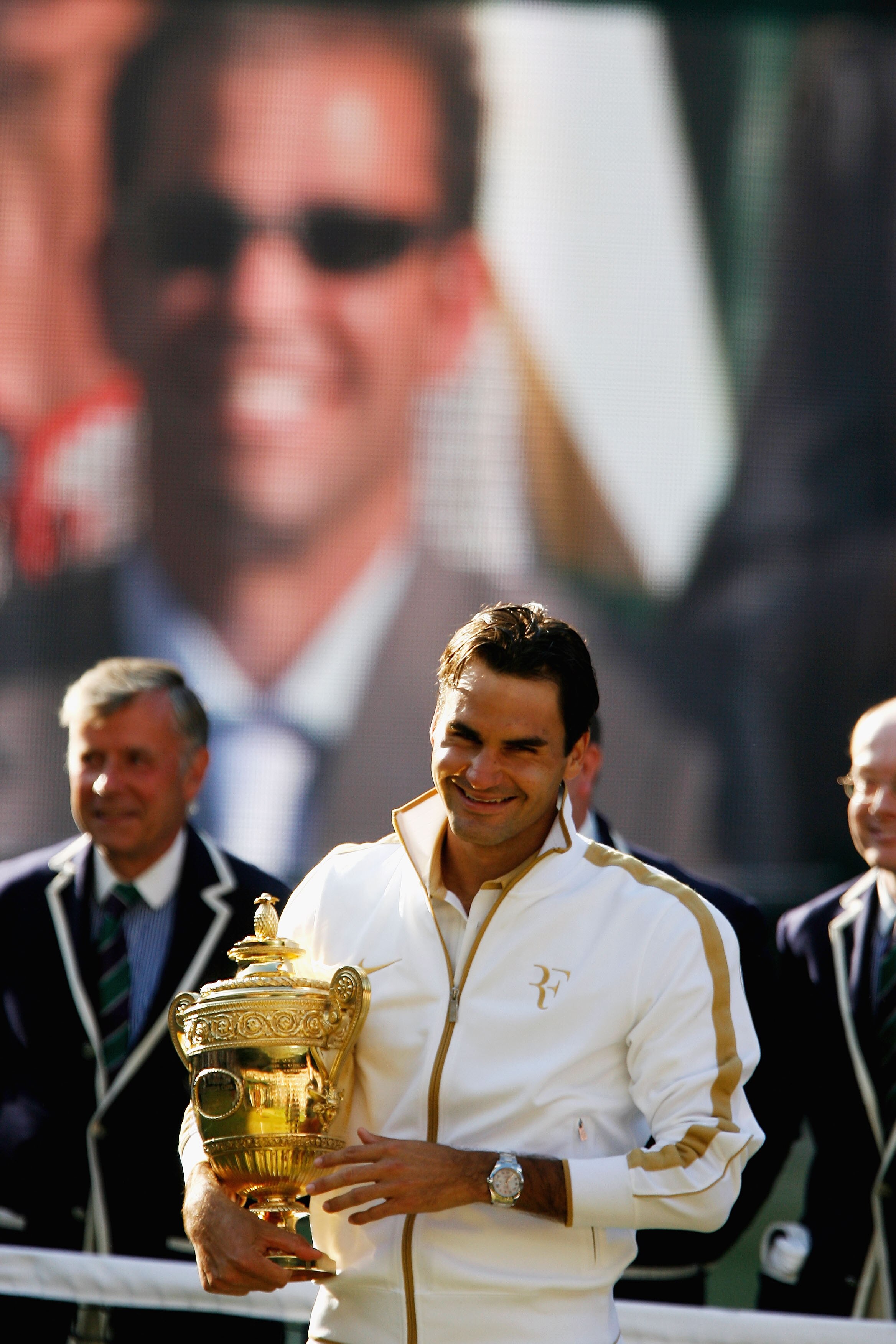 WIMBLEDON, ENGLAND - JULY 05:  Roger Federer of Switzerland celebrates with the trophy as Peter Sampras is shown on the screen after the men's singles final match against Andy Roddick of USA on Day Thirteen of the Wimbledon Lawn Tennis Championships at th