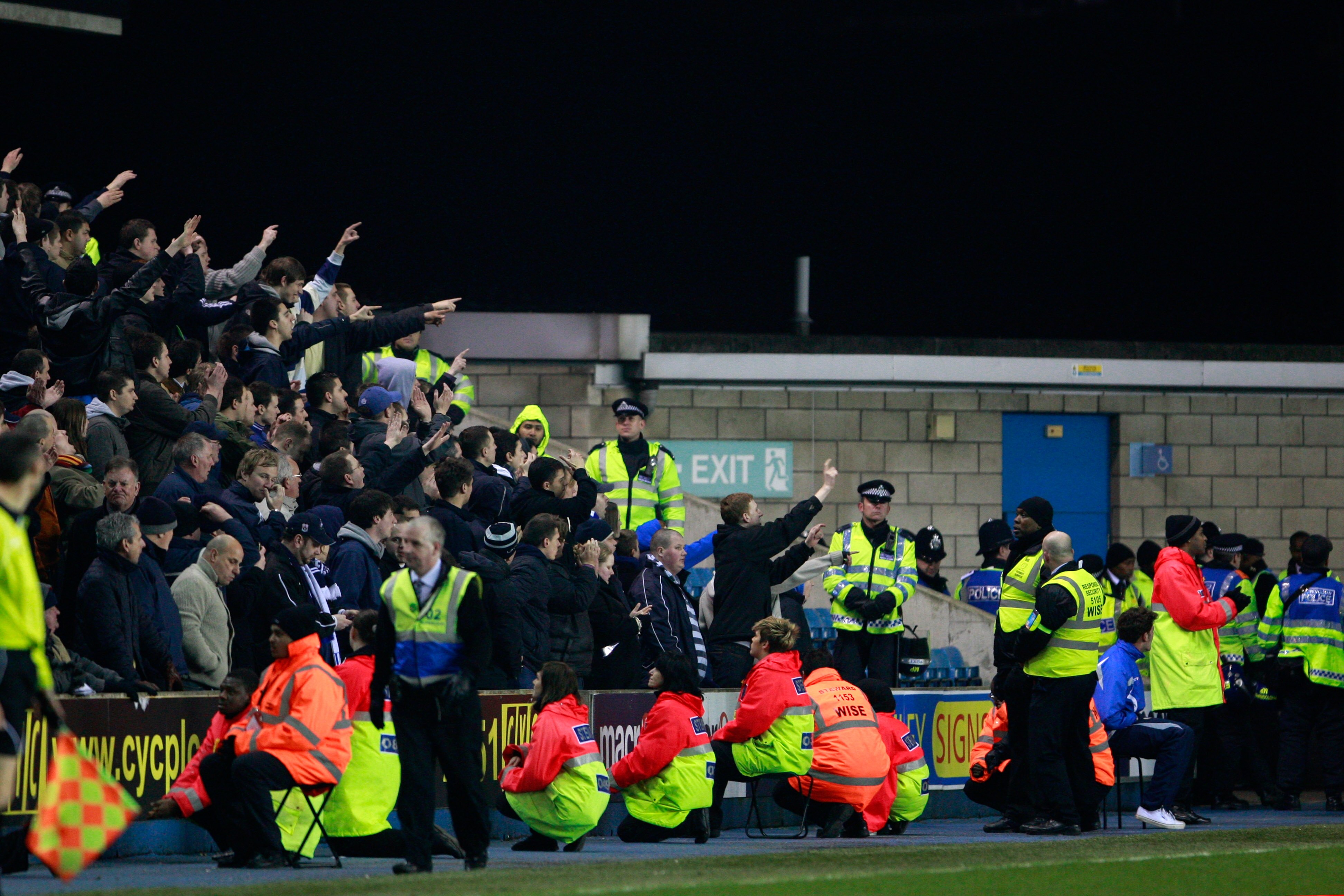 LONDON, ENGLAND - MARCH 08:  Police officers and stewards monitor Millwall supporters as they taunt the away fans during the npower Championship match between Millwall and Queens Park Rangers at The Den on March 8, 2011 in London, England.  (Photo by Dan