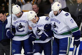 BOSTON, MA - JUNE 13:  Christopher Higgins #20 and Ryan Kesler #17 help Mason Raymond #21 of the Vancouver Canucks off the ice after being checked by Johnny Boychuk #55 of the Boston Bruins in the first period during Game Six of the 2011 NHL Stanley Cup F