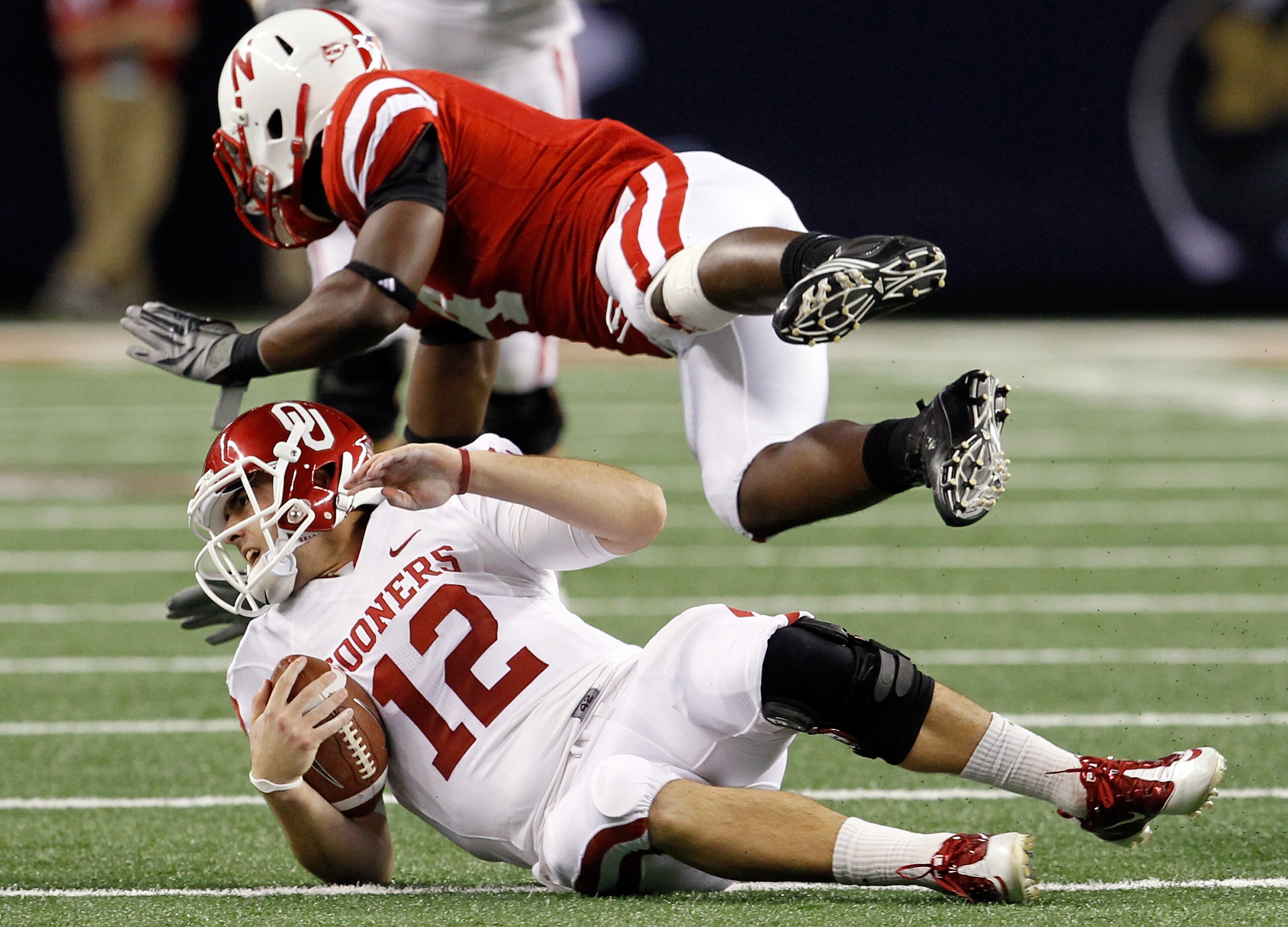 ARLINGTON, TX - DECEMBER 04:  Quarterback Landry Jones #12 of the Oklahoms Sooners slides to the turf after scrambling for a gain against Linebacker Lavonte David #4 of the Nebraska Cornhuskers at Cowboys Stadium on December 4, 2010 in Arlington, Texas.
