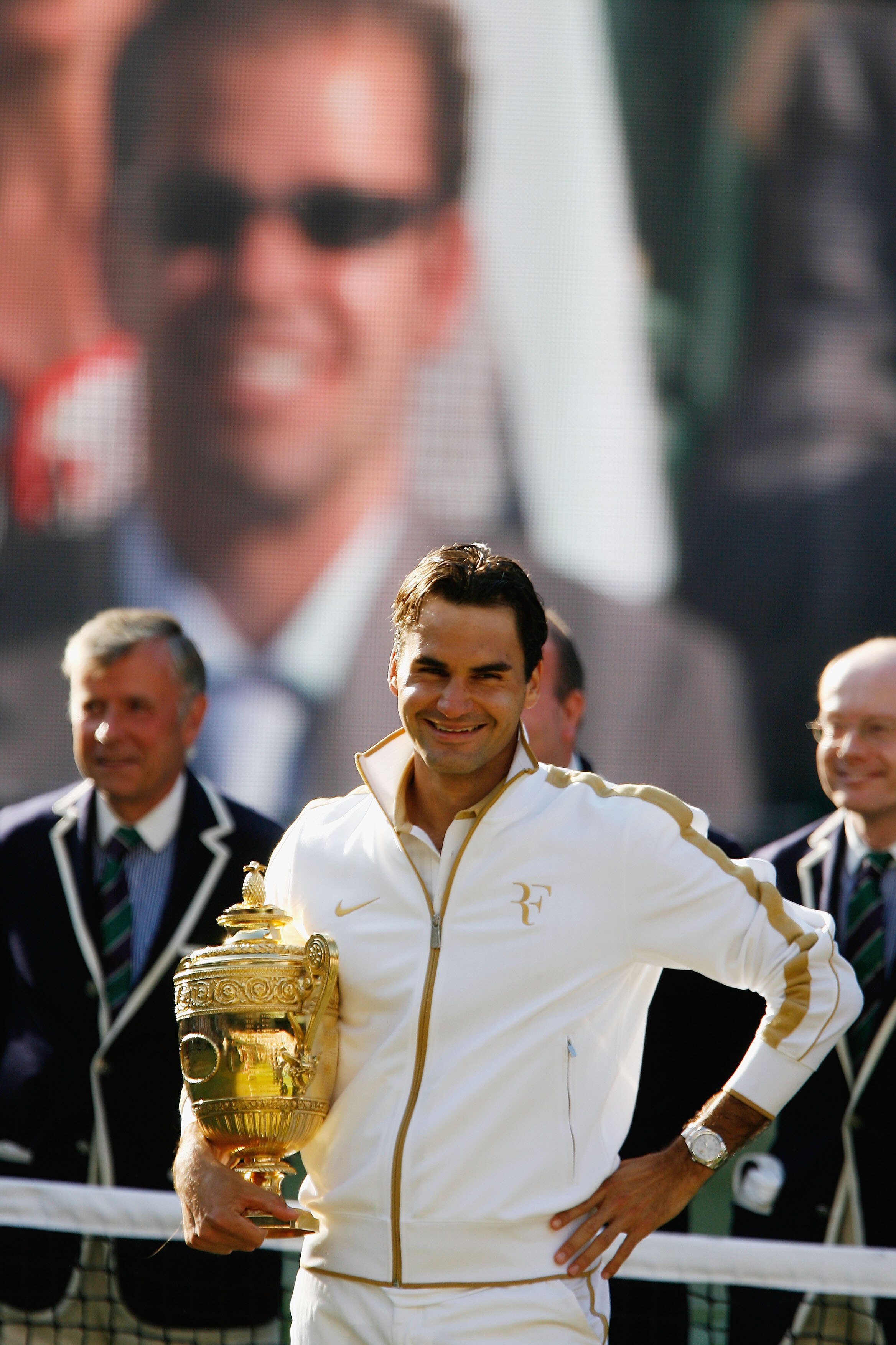 WIMBLEDON, ENGLAND - JULY 05:  Roger Federer of Switzerland celebrates with the trophy as Peter Sampras is shown on the screen after the men's singles final match against Andy Roddick of USA on Day Thirteen of the Wimbledon Lawn Tennis Championships at th