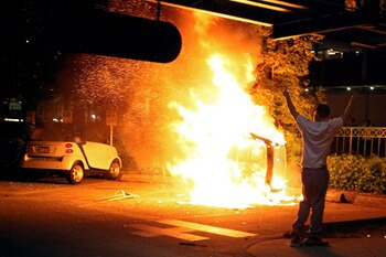 VANCOUVER, BC - JUNE 15:  A person walks in front of a burning vehicle on June 15, 2011 in Vancouver, Canada. Vancouver broke out in riots after their hockey team the Vancouver Canucks lost in Game Seven of the Stanley Cup Finals.  (Photo by Elsa/Getty Im