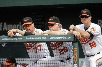 BALTIMORE, MD - JUNE 05:  Manager Buck Showalter #26 of the Baltimore Orioles watches from the dugout with coaches John Russell #77 and Jim Presley #16 against the Toronto Blue Jays at Oriole Park at Camden Yards on June 5, 2011 in Baltimore, Maryland.  (