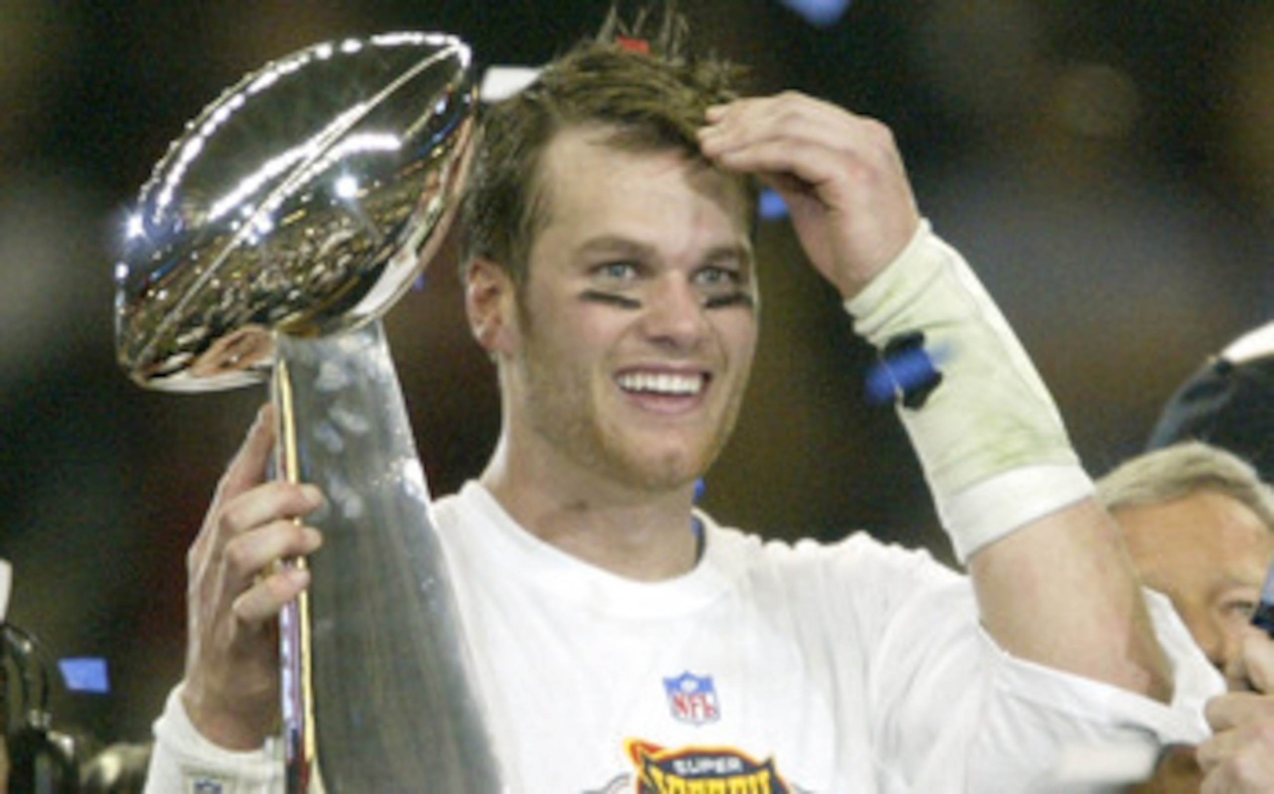 HOUSTON, TX - FEBRUARY 1:  MVP Tom Brady #12 of the New England Patriots raises the Lombardi trophy as he is interviewed by television commentator Jim Nance after defeating the Carolina Panthers 32-29 in Super Bowl XXXVIII at Reliant Stadium on February 1