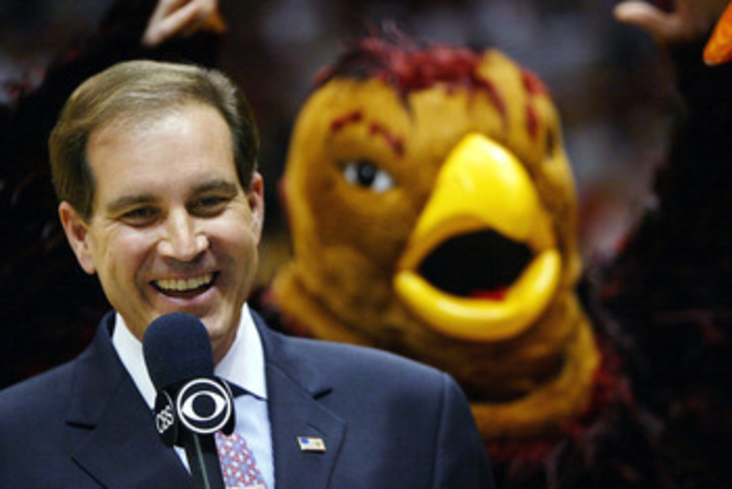 EAST RUTHERFORD, NJ - MARCH 27: CBS analyst Jim Nantz shows a smile as the St. Joseph's Hawks mascot flaps his arms in the background before the start of the fourth round regional game of the NCAA Division I Men's Basketball Tournament against Oklahoma S EAST RUTHERFORD, NJ - MARCH 27: CBS analyst Jim Nantz shows a smile as the St. Joseph's Hawks mascot flaps his arms in the background before the start of the fourth round regional game of the NCAA Division I Men's Basketball Tournament against Oklahoma S
