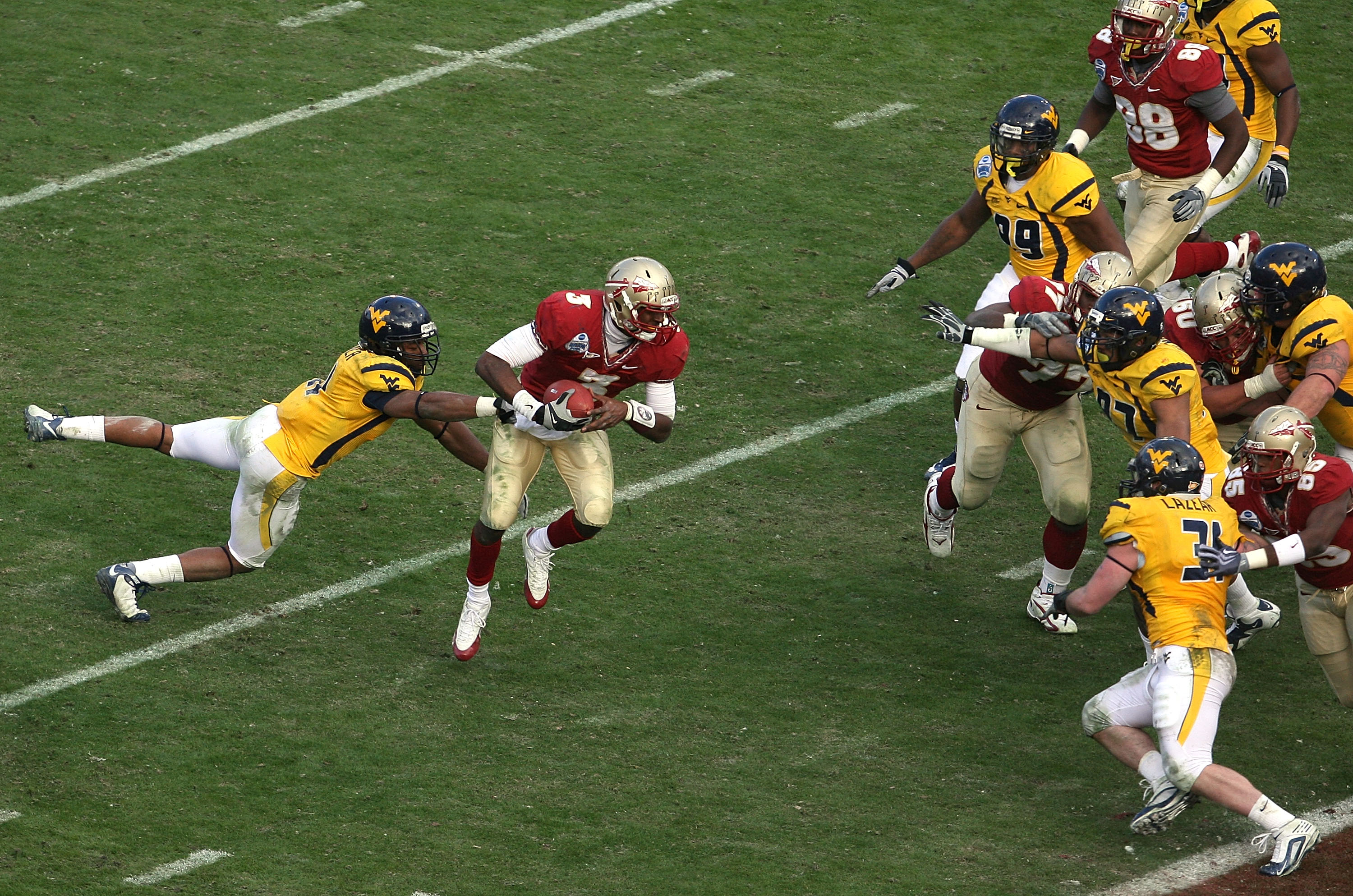 JACKSONVILLE, FL - JANUARY 01:  Quarterback E.J. Manuel #3 of the Florida State Seminoles avoids a tackle by defensive back Sidney Glover #11 of the West Virginia Mountaineers on his way to a touchdown run during the Konica Minolta Gator Bowl on January 1