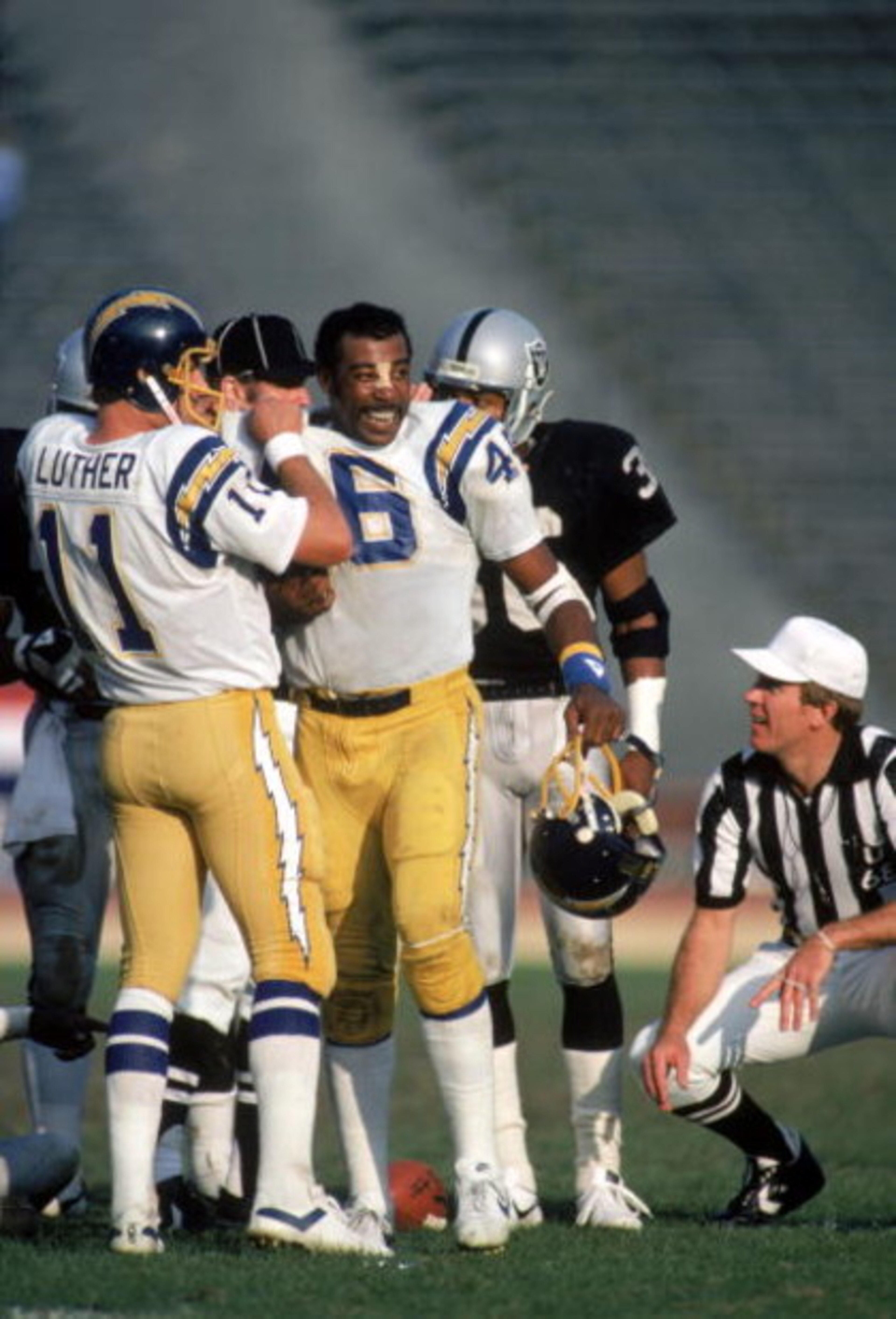LOS ANGELES - DECEMBER 18: Quarterback Ed Luther #11 of the San Diego Chargers tucks the shoulder pads into the jersey of teammate Chuck Muncie #46 during a game against the Los Angeles Raiders at the Los Angeles Memorial Coliseum on December 18, 1983 in LOS ANGELES - DECEMBER 18: Quarterback Ed Luther #11 of the San Diego Chargers tucks the shoulder pads into the jersey of teammate Chuck Muncie #46 during a game against the Los Angeles Raiders at the Los Angeles Memorial Coliseum on December 18, 1983 in