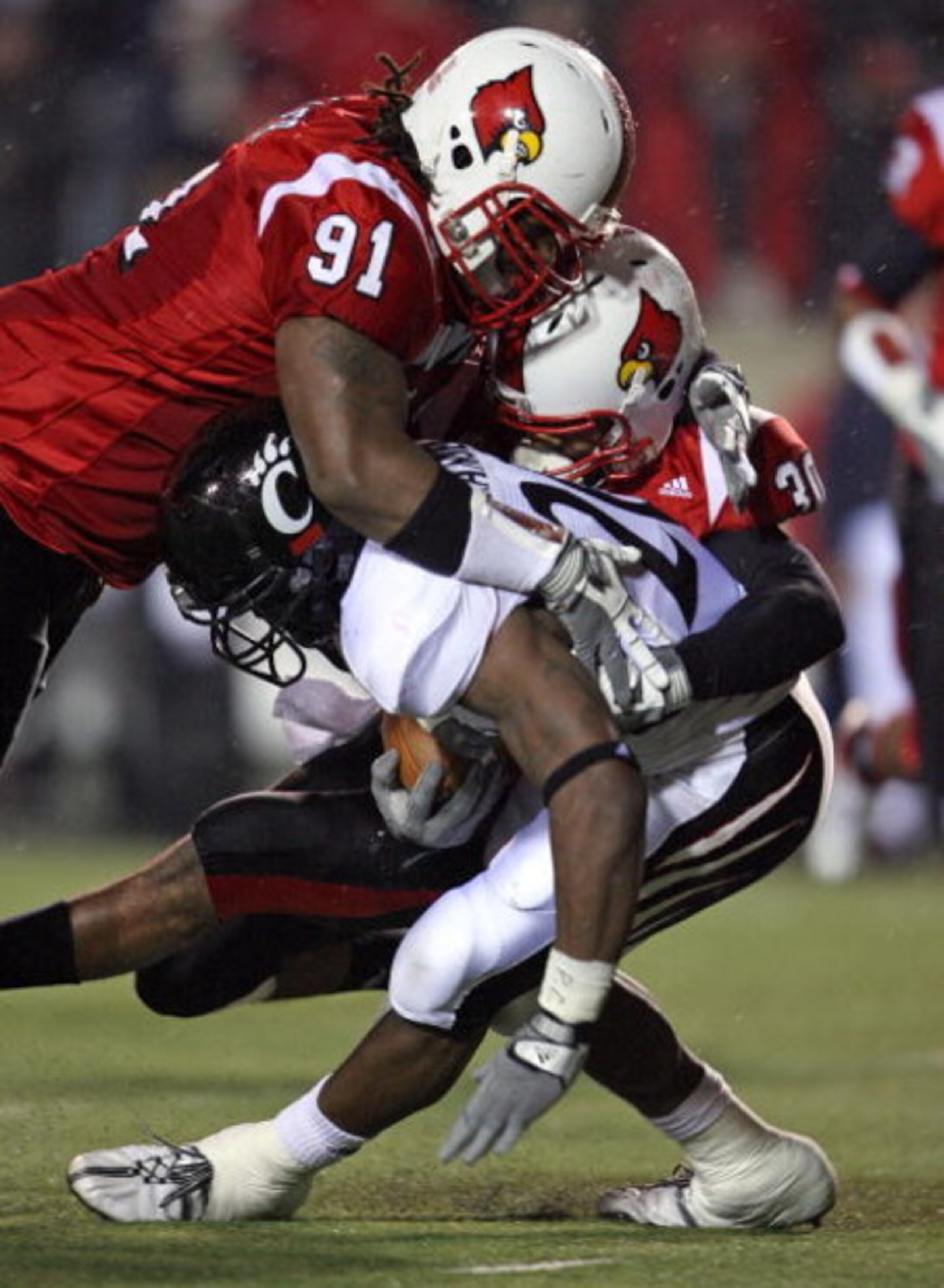 LOUISVILLE, KY - NOVEMBER 14:  L.T. Walker #91 and Daniel Covington #30 of the Louisville Cardinals tackle Jacob Ramsey #20 of the Cincinnati Bearcats during the Big East Conference game against  on November 14, 2008 at  Papa John's Stadium in Louisville,