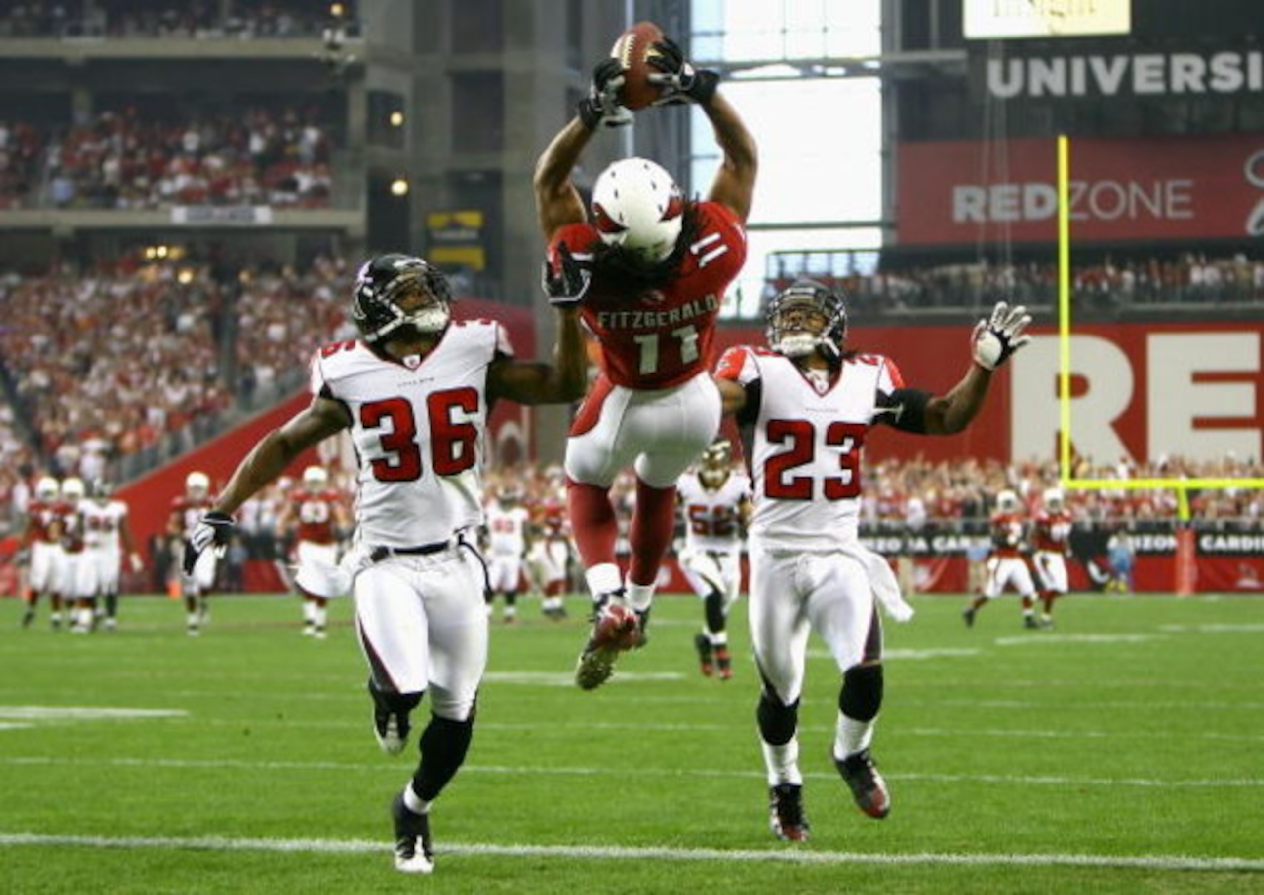 GLENDALE, AZ - JANUARY 03:  Wide receiver Larry Fitzgerald #11 of the Arizona Cardinals makes a leaping 42 yard touchdown reception over Lawyer Milloy #36 and Chris Houston #23 of the Atlanta Falcons during the first quarter of the NFC Wild Card Game on J