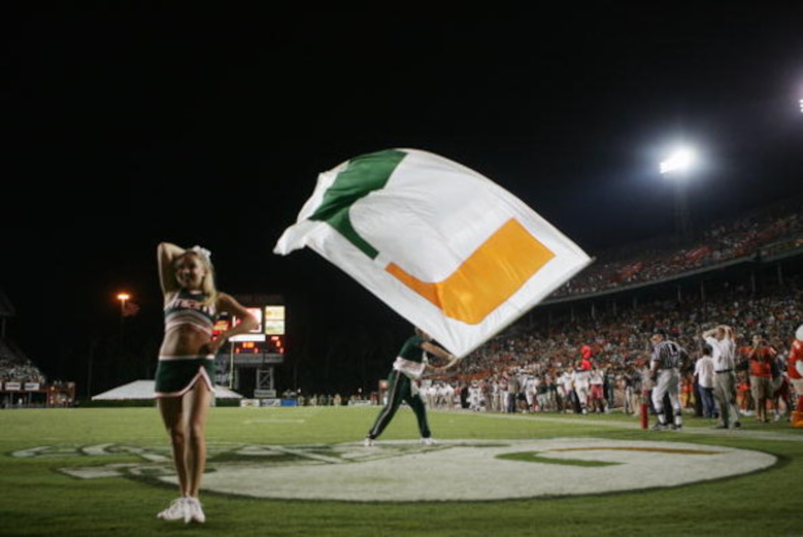 MIAMI - OCTOBER 14:  A male Miami Hurricanes cheerleader waves a giant flag while a female cheerleader performs during the game against the Florida International Panthers at the Orange Bowl on October 14, 2006 in Miami, Florida. Miami won 35-0.  (Photo by