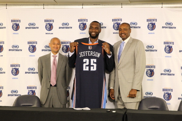 CHARLOTTE, NC - JULY 10:  Al Jefferson #25 of the Charlotte Bobcats poses with his uniform alongside General Manager Rich Cho and President of Basketball Operations Rod Higgins during his intro to the media at the Time Warner Cable Arena on July 10, 2013 