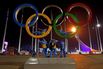 SOCHI, RUSSIA - FEBRUARY 07:  People pose for a photo on the Olympic Rings as the Olympic Cauldron burns in the background on February 7, 2014 in Sochi, Russia.  (Photo by Michael Heiman/Getty Images)