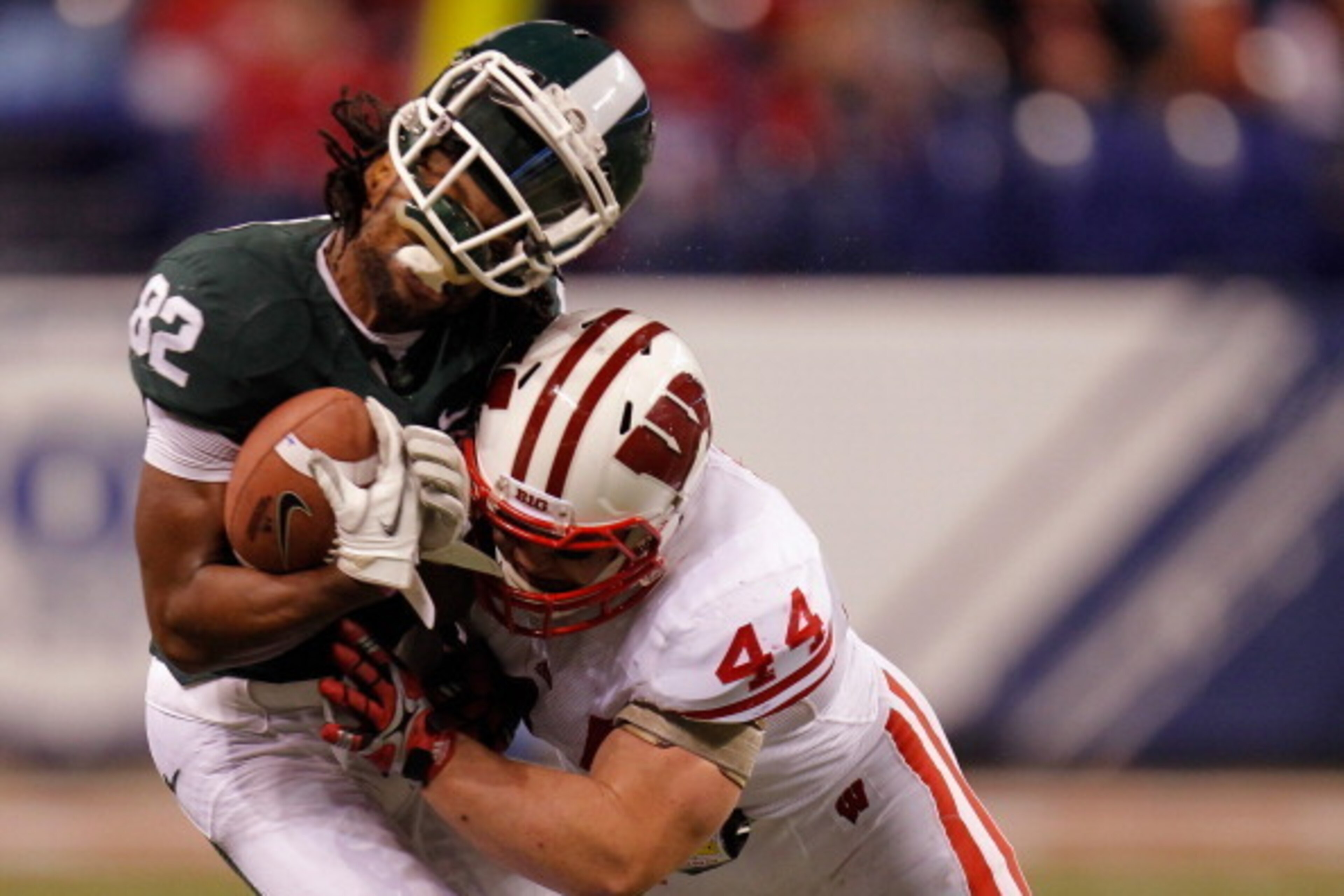 INDIANAPOLIS, IN - DECEMBER 03:  Keshawn Martin #82 of the Michigan State Spartans loses his helmet as he is hit by Chris Borland #44 of the Wisconsin Badgers during the third quarter of the Big 10 Conference Championship Game at Lucas Oil Stadium on Dece
