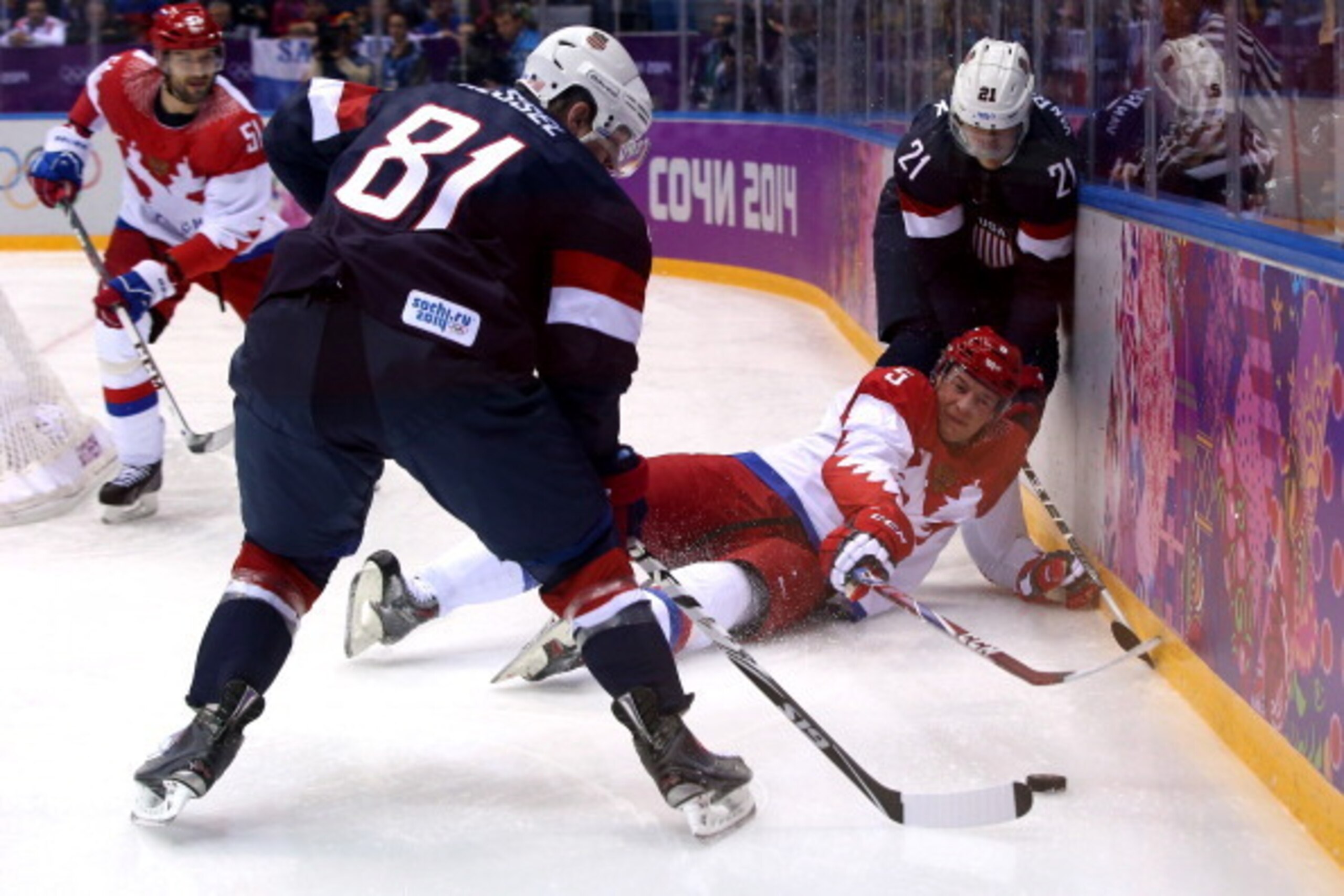 SOCHI, RUSSIA - FEBRUARY 15:  Ilya Nikulin #5 of Russia falls to the ice against Phil Kessel #81 and James van Riemsdyk #21 of United States during the Men's Ice Hockey Preliminary Round Group A game on day eight of the Sochi 2014 Winter Olympics at Bolsh