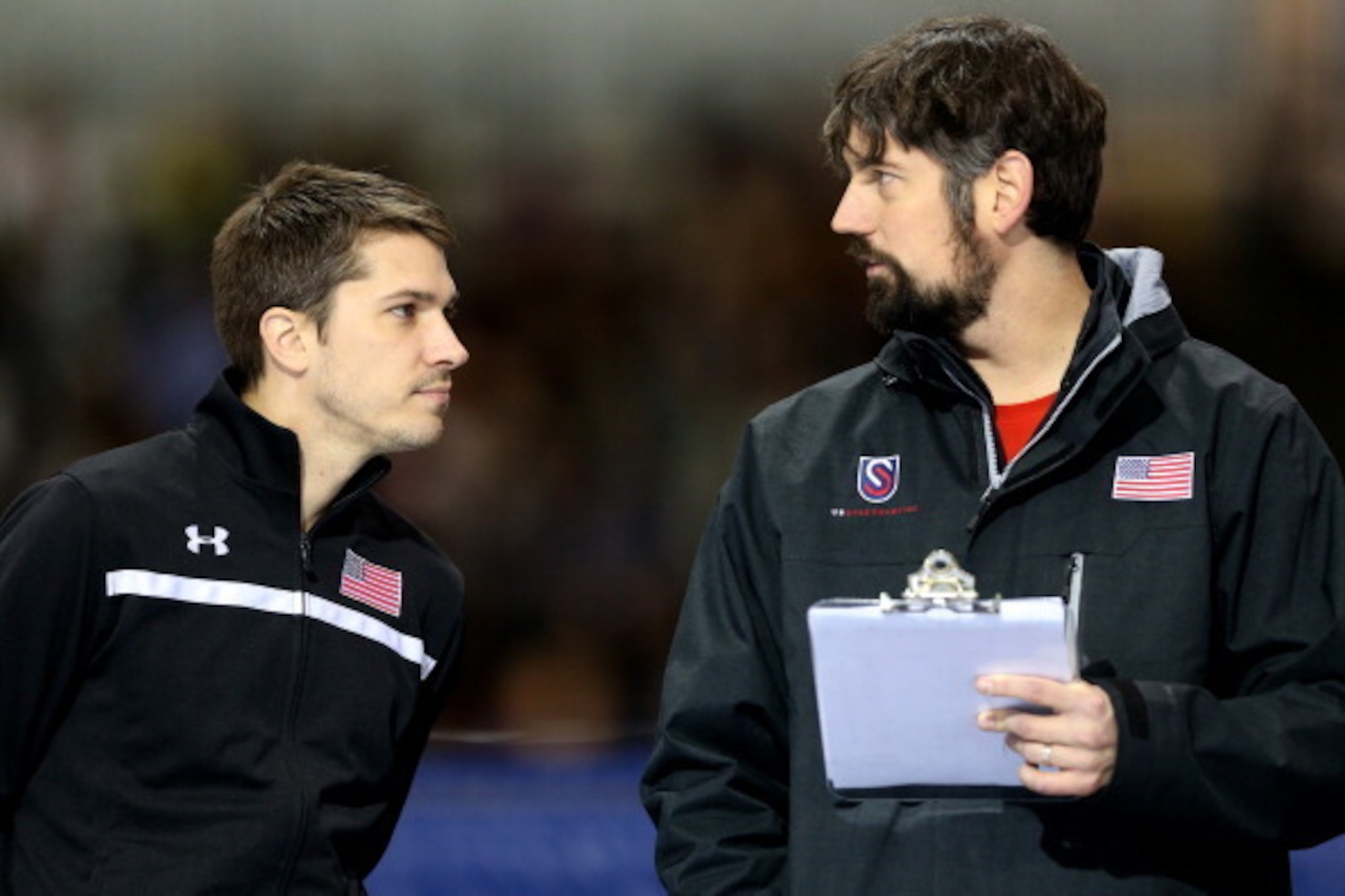 SALT LAKE CITY, UT - DECEMBER 28:  Kip Carpenter, national all around head coach, confers with Matt Kooreman, national training center coach, on the sidelines duirng the men's 500 meter during the U.S. Speed Skating Long Track Olympic Trials at the Utah O