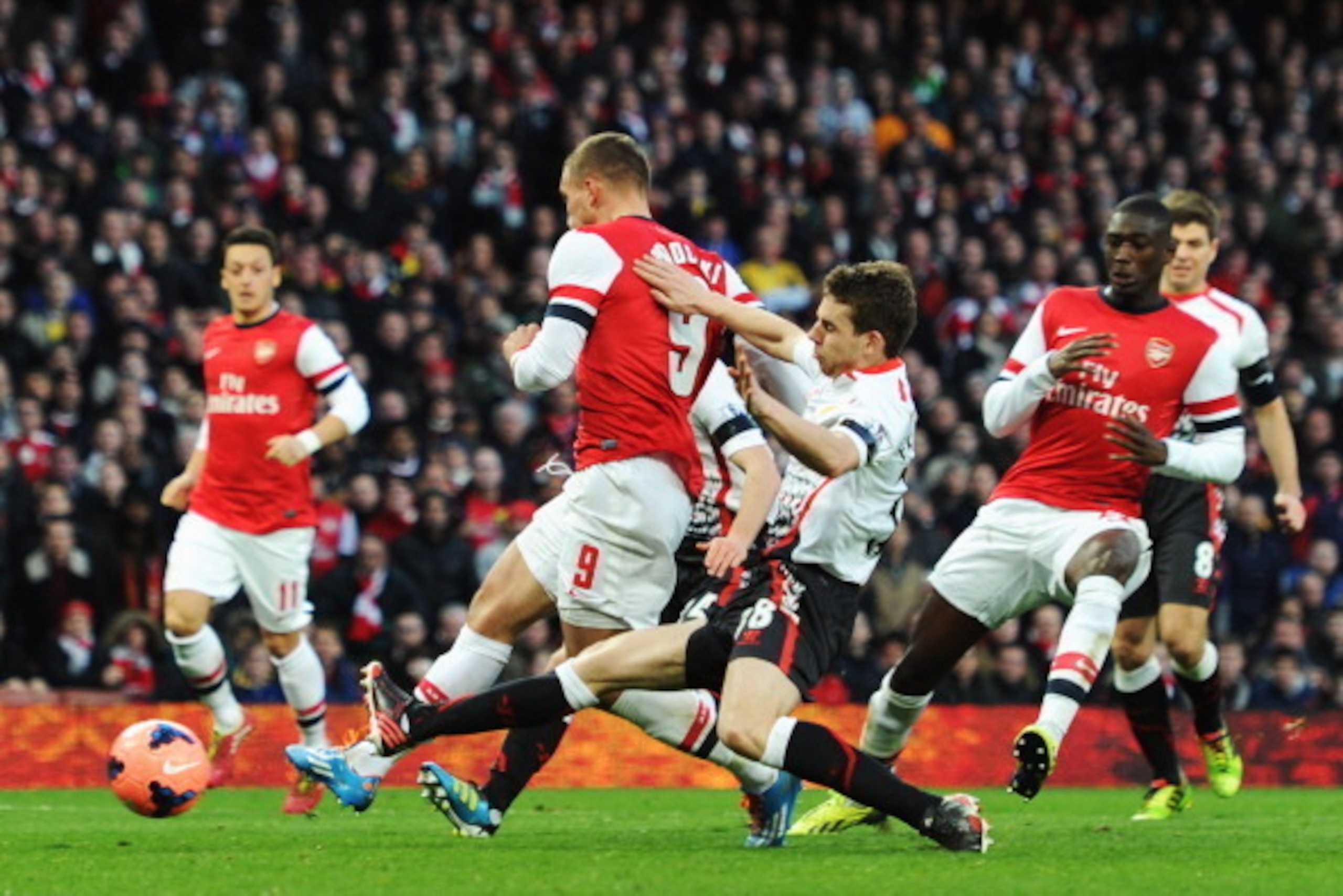 LONDON, ENGLAND - FEBRUARY 16: Lukas Podolski (C) of Arsenal gets his shot in under pressure to score his sides second goal during the FA Cup Fifth Round match between Arsenal and Liverpool at the Emirates Stadium on February 16, 2014 in London, England. LONDON, ENGLAND - FEBRUARY 16: Lukas Podolski (C) of Arsenal gets his shot in under pressure to score his sides second goal during the FA Cup Fifth Round match between Arsenal and Liverpool at the Emirates Stadium on February 16, 2014 in London, England.