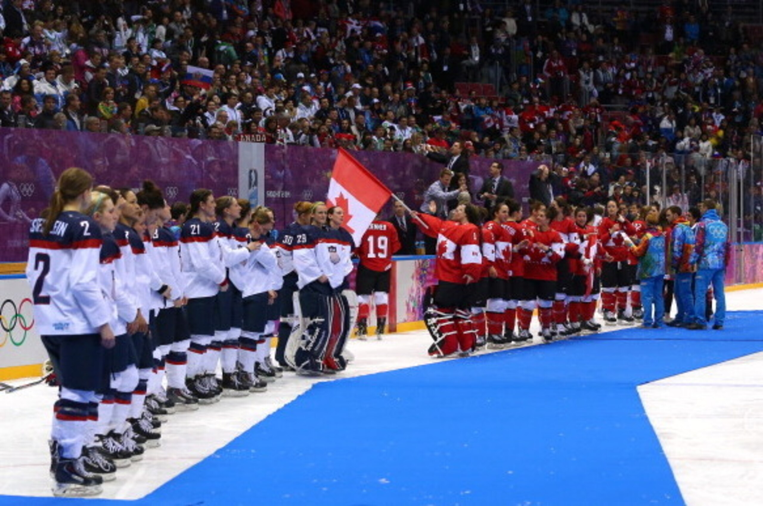 SOCHI, RUSSIA - FEBRUARY 20:  (L-R) Silver medalists the United States and gold medalists Canada celebrate during the flower ceremony for the Ice Hockey Women's Gold Medal Game on day 13 of the Sochi 2014 Winter Olympics at Bolshoy Ice Dome on February 20