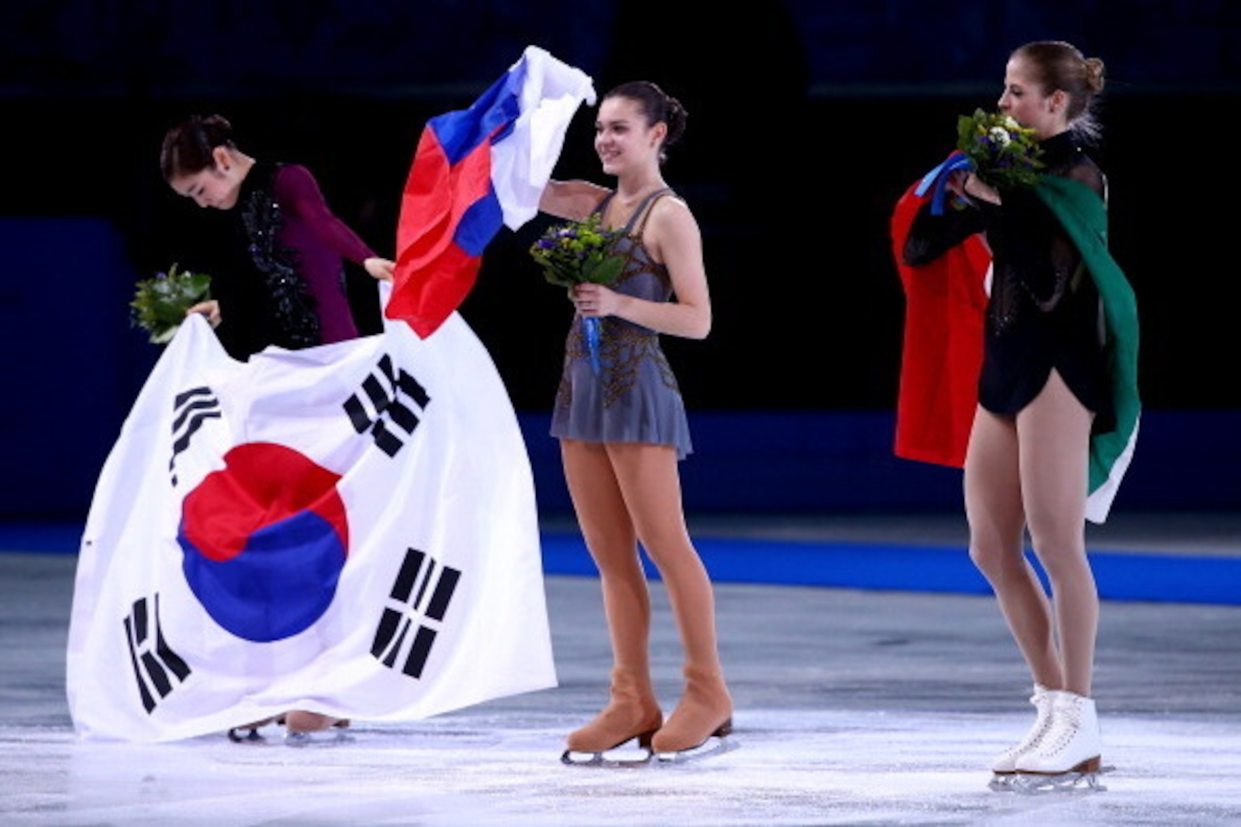 SOCHI, RUSSIA - FEBRUARY 20:  (L-R) Silver medalist Yuna Kim of South Korea, gold medalist Adelina Sotnikova of Russia and bronze medalist Carolina Kostner of Italy celebrate during the flower ceremony for the Ladies' Figure Skating on day 13 of the Sochi