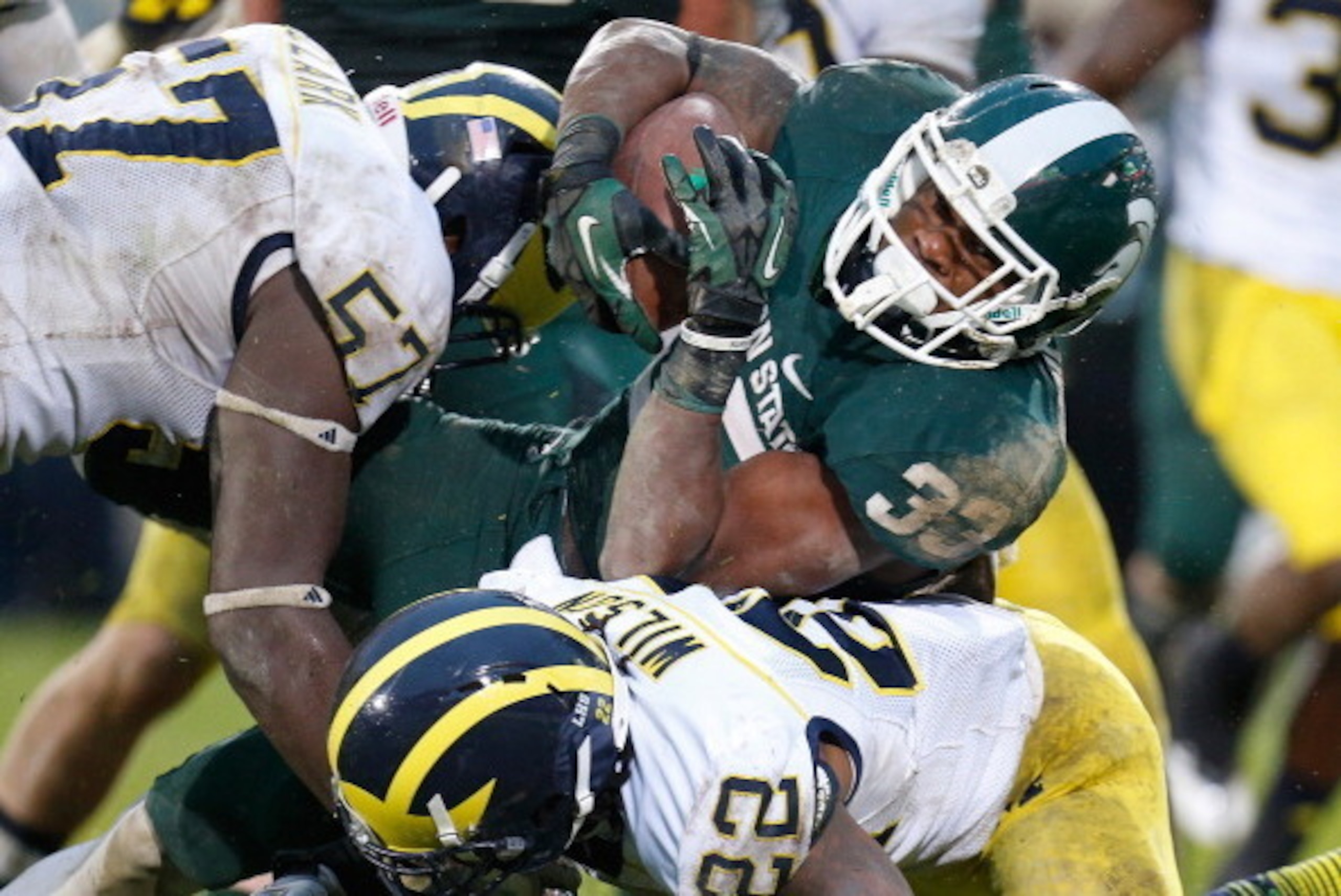 EAST LANSING, MI - NOVEMBER 02:  Frank Clark #57 and Jarrod Wilson #22 of the Michigan Wolverines bring down Jeremy Langford #33 of the Michigan State Spartans  in the fourth quarter at Spartan Stadium on November 2, 2013 in East Lansing, Michigan. Michig