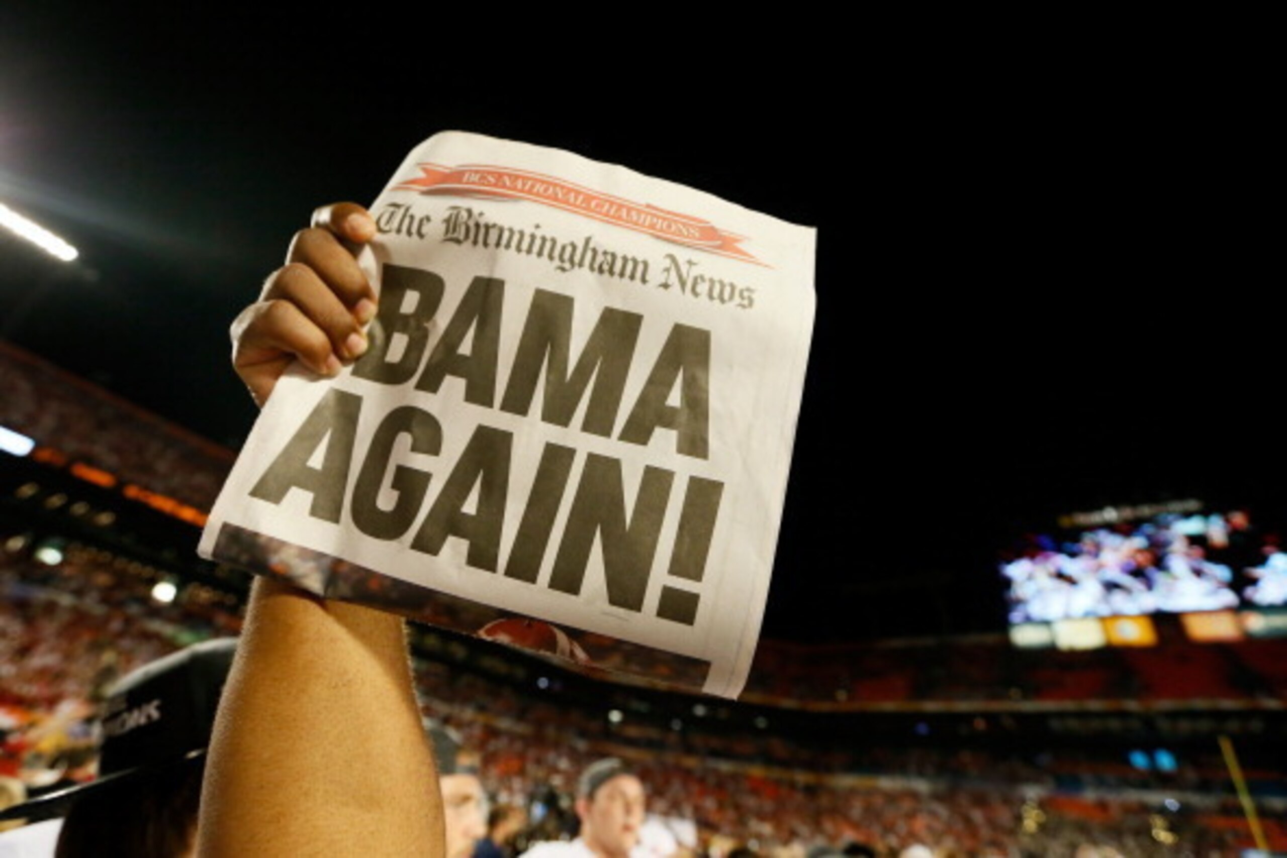 MIAMI GARDENS, FL - JANUARY 07:  A member of the Alabama Crimson Tide holds up a newpaper front page with a headline reading 'Bama Again!' after they defeated the Notre Dame Fighting Irish by a score of 42-14 to win the 2013 Discover BCS National Champion