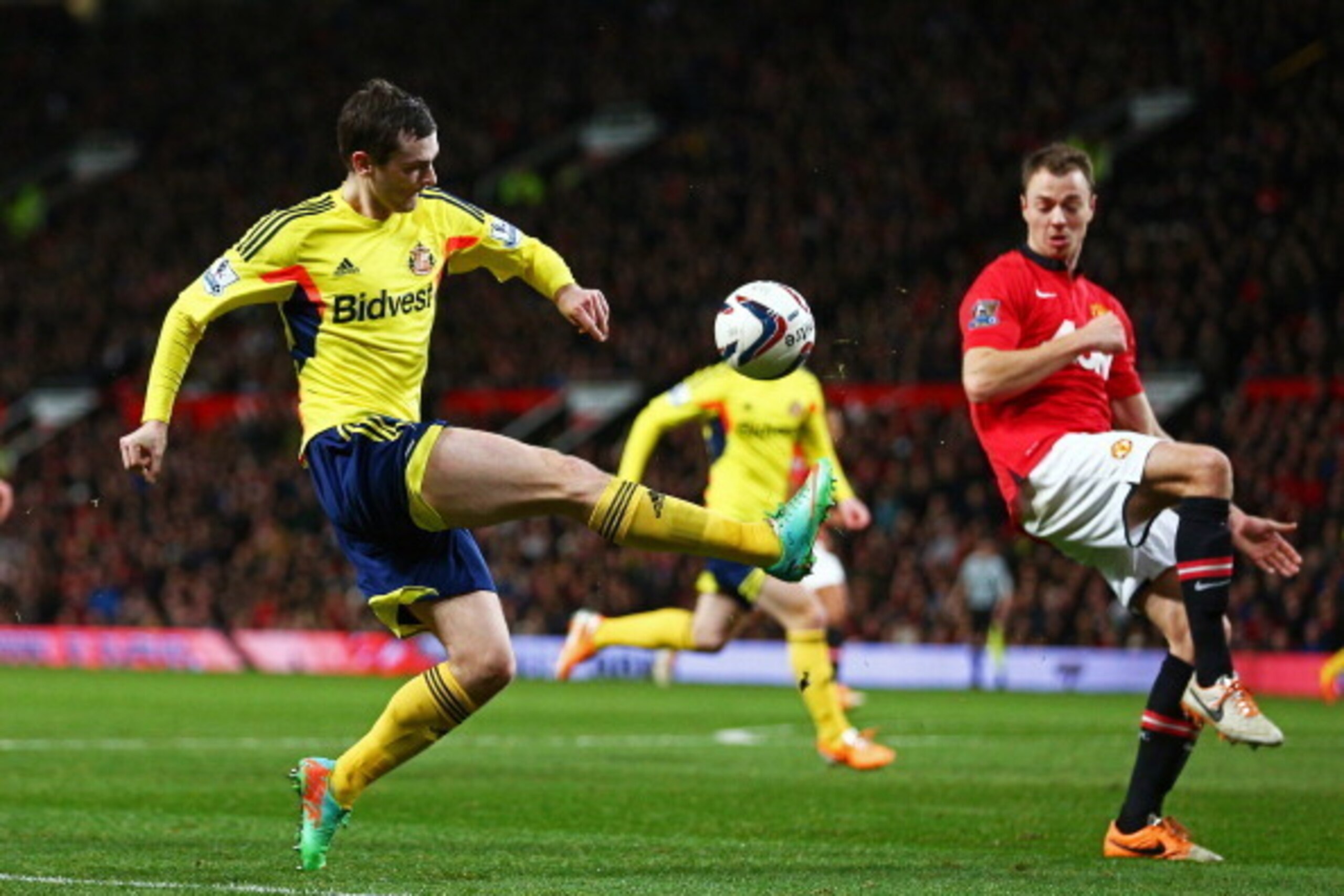 MANCHESTER, ENGLAND - JANUARY 22:  Adam Johnson of Sunderland crosses the ball as Jonny Evans of Manchester United closes in during the Capital One Cup semi final, second leg match between Manchester United and Sunderland at Old Trafford on January 22, 20