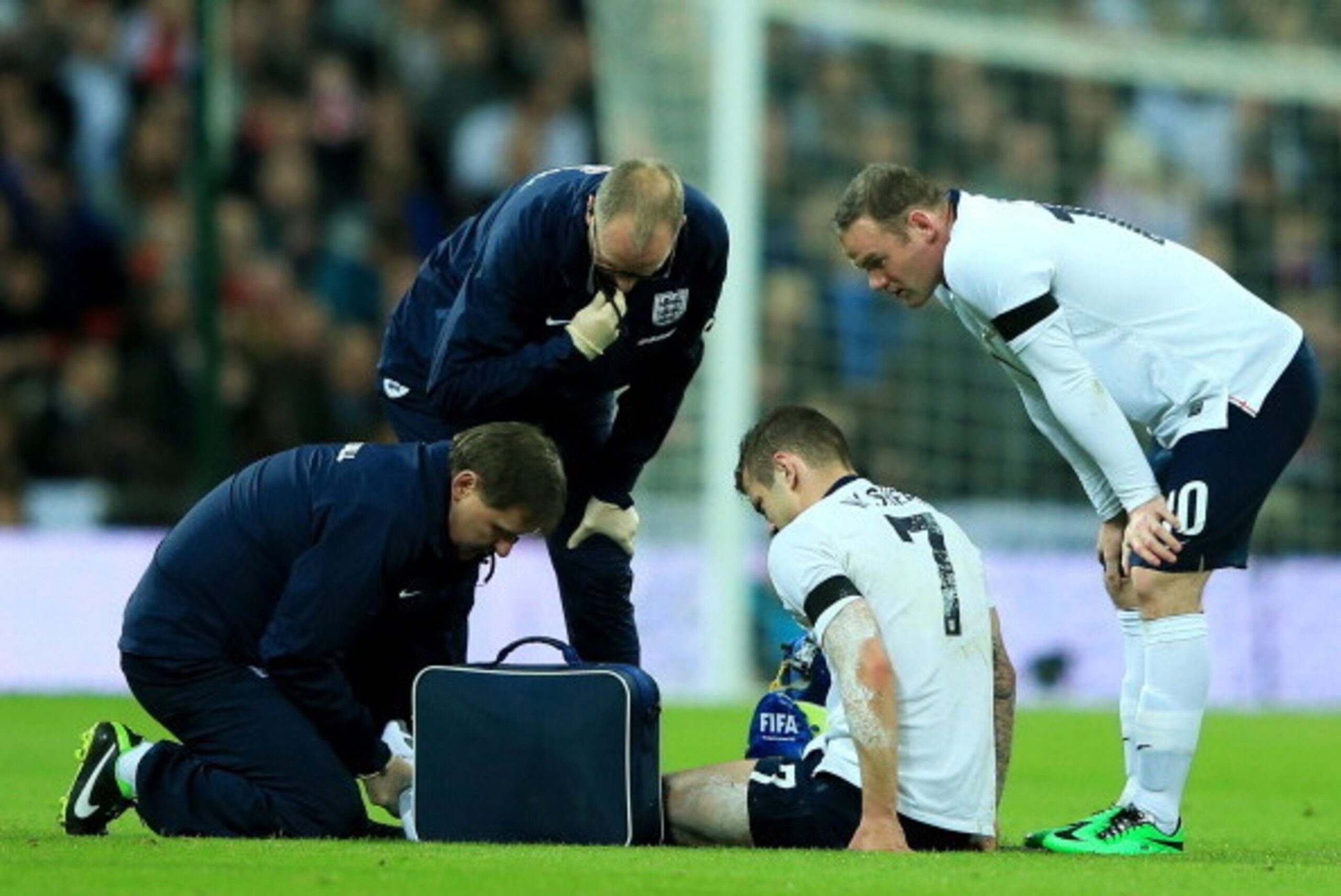 LONDON, ENGLAND - MARCH 05:  Wayne Rooney of England looks on as injured team mate Jack Wilshere is given treatment during the International Friendly match between England and Denmark at Wembley Stadium on March 5, 2014 in London, England.  (Photo by Rich