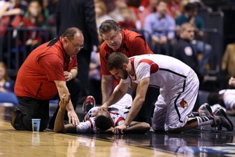 INDIANAPOLIS, IN - MARCH 31:  Kevin Ware #5 of the Louisville Cardinals talks with teammate Luke Hancock #11  as Ware is tended to by medical personnel after he injured his leg in the first half against the Duke Blue Devils during the Midwest Regional Fin