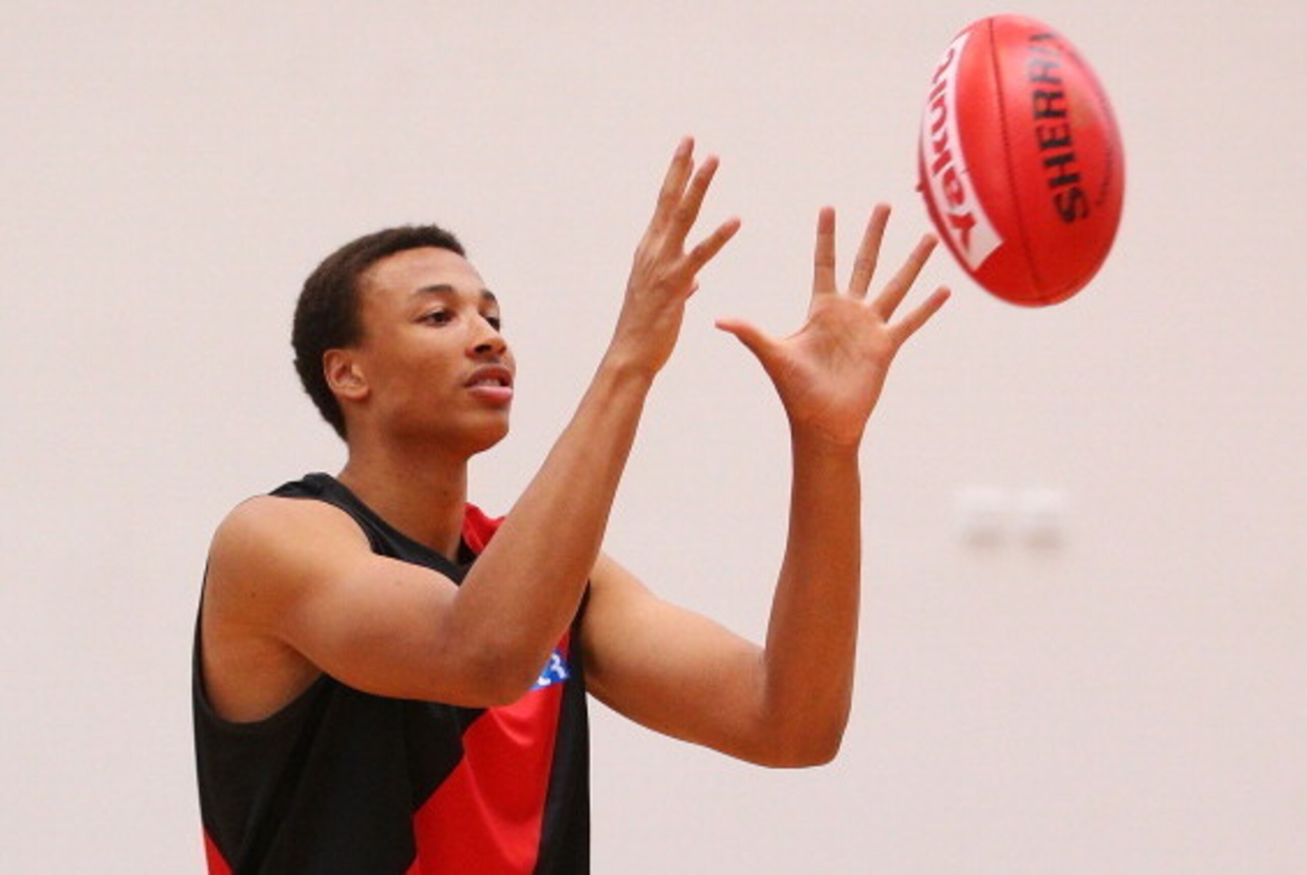 MELBOURNE, AUSTRALIA - FEBRUARY 14:  Young Australian basketball player Dante Exum marks the ball after being presented a jumper by Joe Daniher of the Bombers during an Essendon Bombers AFL media session at True Value Solar Centre on February 14, 2014 in 
