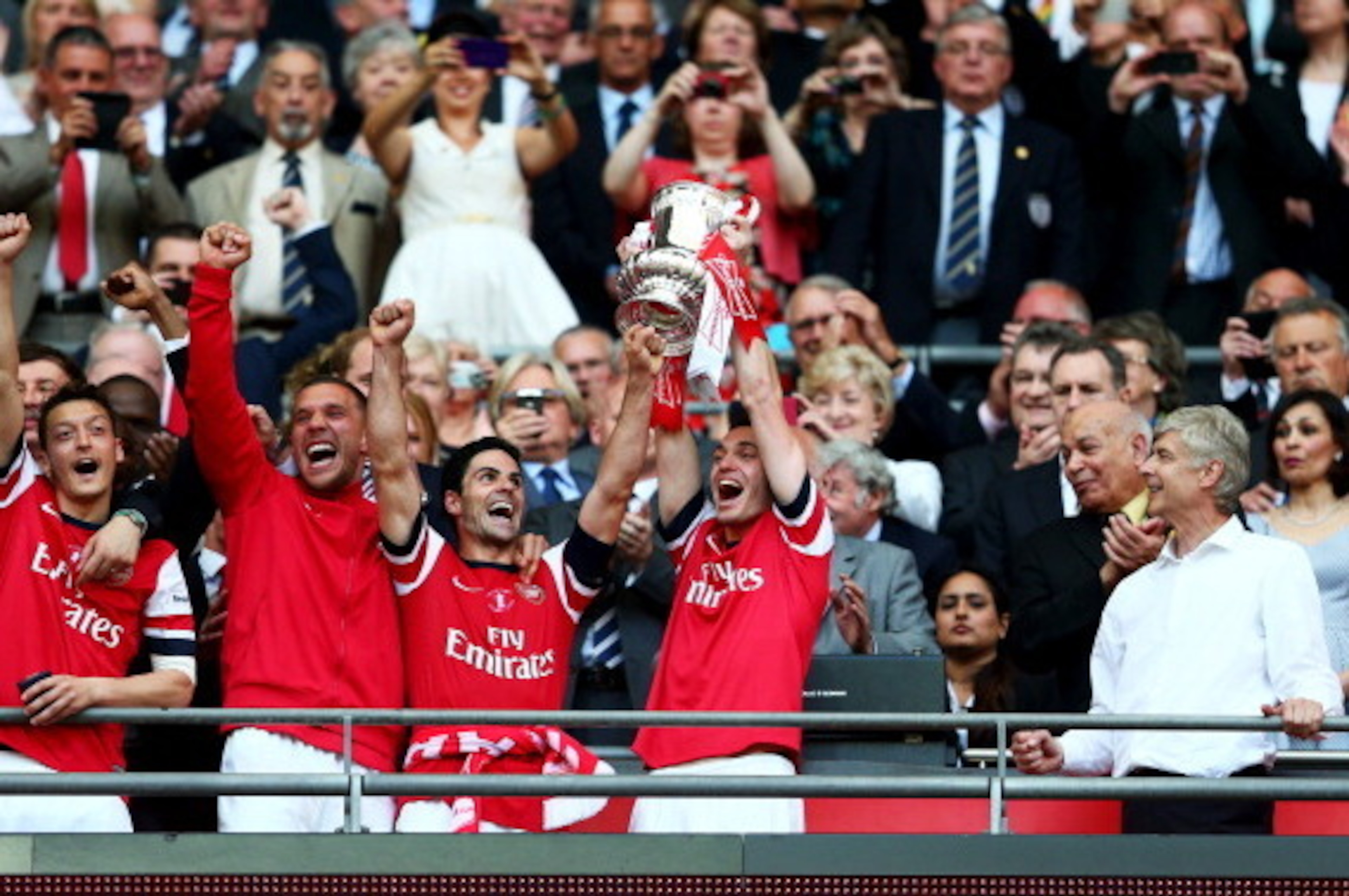 LONDON, ENGLAND - MAY 17:  Captain Thomas Vermaelen of Arsenal (2R) lifts the trophy in celebration as Arsene Wenger manager of Arsenal (R) looks on after the FA Cup with Budweiser Final match between Arsenal and Hull City at Wembley Stadium on May 17, 20