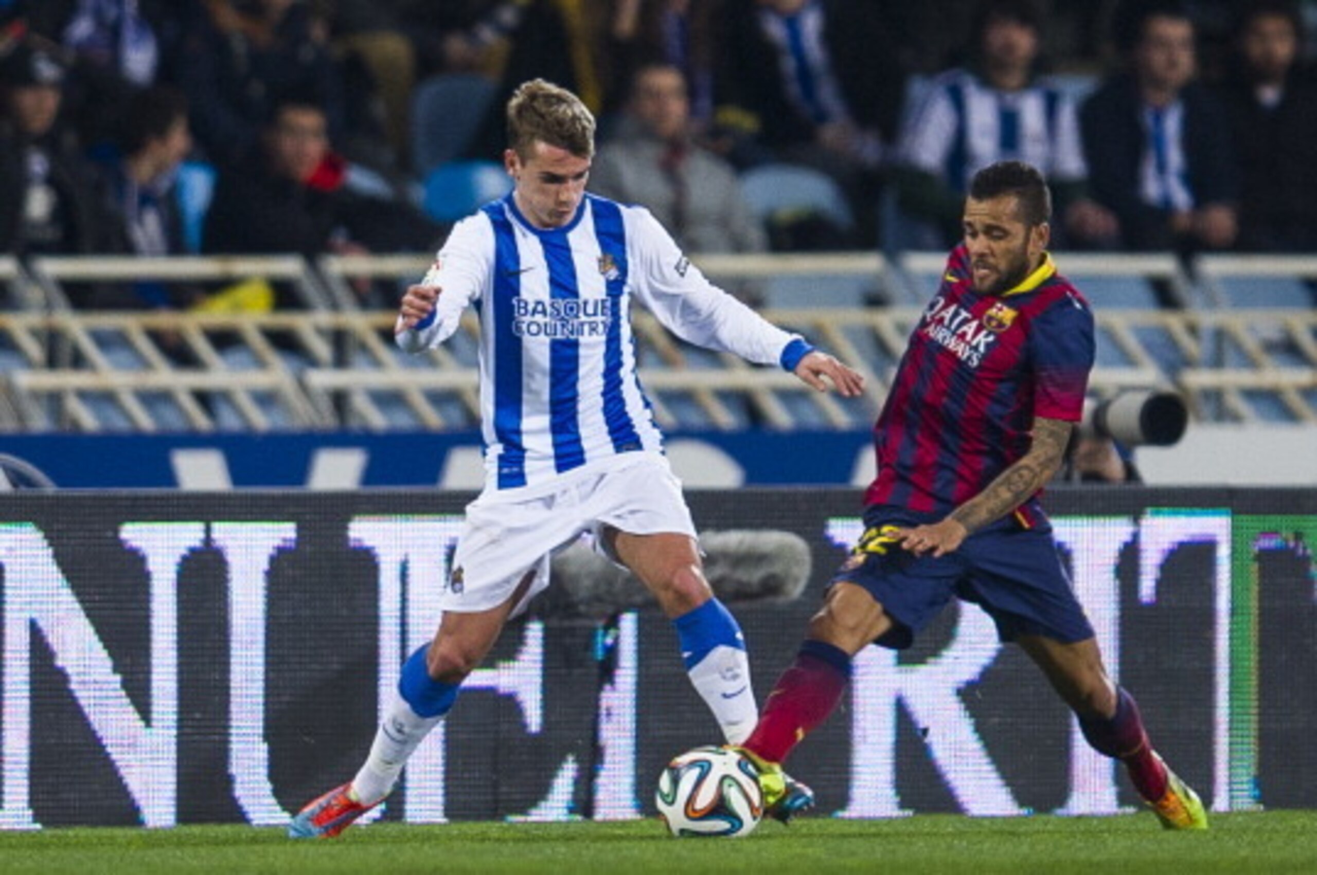 SAN SEBASTIAN, SPAIN - FEBRUARY 12:  Dani Alves of FC Barcelona duels for the ball with Antoine Griezmann of Real Sociedad during the Copa del Rey Semi-Final first leg match between Real Sociedad and Barcelona at Estadio Anoeta  on February 12, 2014 in Sa
