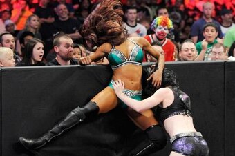 Paige sends Alicia Fox into the barricade outside the ring.