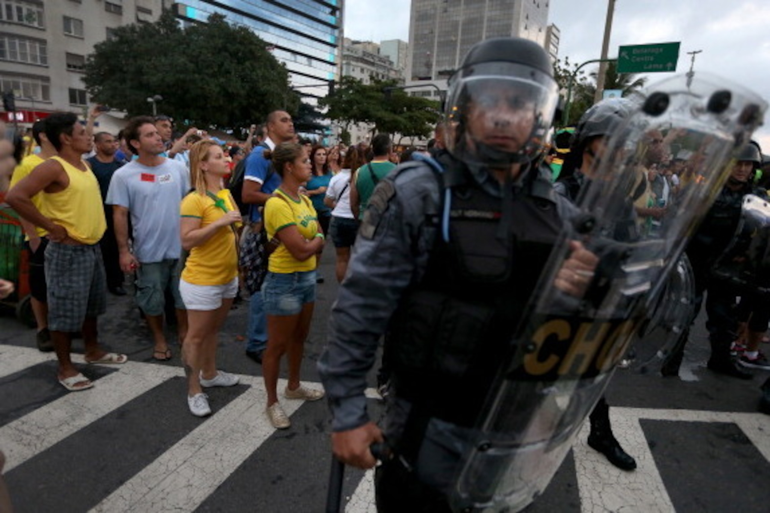 RIO DE JANEIRO, BRAZIL - JUNE 12: People watch the World Cup match on giant screens setup at the FIFA fan fest from behind riot police as anti-World Cup protesters pass by on Copacabana beach on June 12, 2014 in Rio de Janeiro, Brazil. Brazil defeated C RIO DE JANEIRO, BRAZIL - JUNE 12: People watch the World Cup match on giant screens setup at the FIFA fan fest from behind riot police as anti-World Cup protesters pass by on Copacabana beach on June 12, 2014 in Rio de Janeiro, Brazil. Brazil defeated C