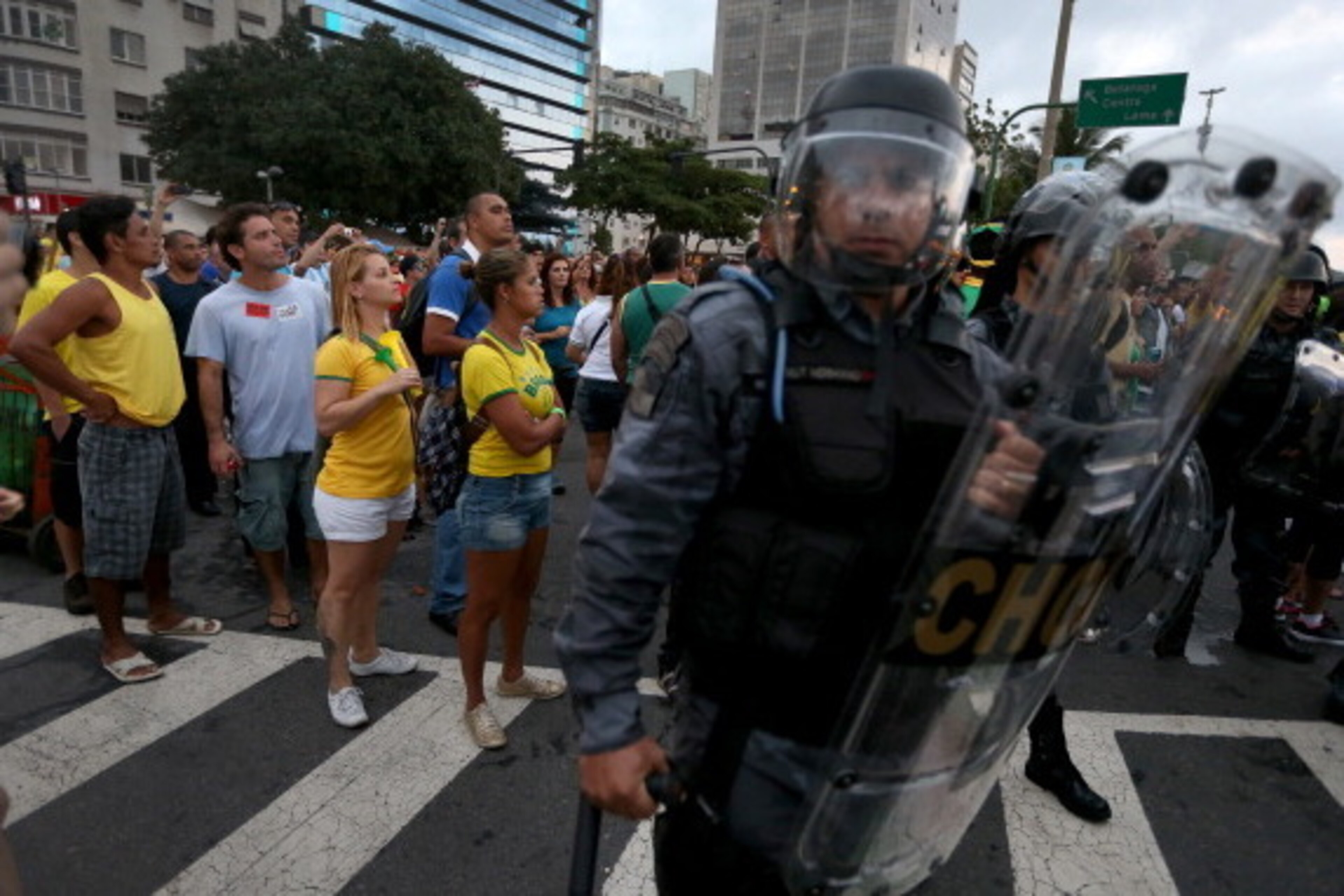 RIO DE JANEIRO, BRAZIL - JUNE 12:  People watch the World Cup match on giant screens setup at the FIFA fan fest from behind riot police as anti-World Cup protesters pass by on Copacabana beach on June 12, 2014 in Rio de Janeiro, Brazil.  Brazil defeated C