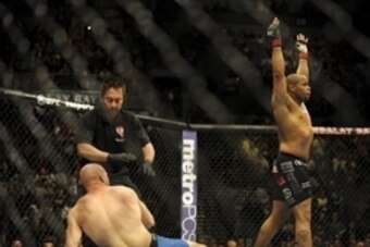 Feb 22, 2014; Las Vegas, NV, USA; Patrick Cummins (blue gloves) throws his hands up as Daniel Cormier lies on the mat after the referee stops their UFC light heavyweight bout at Mandalay Bay. Cormier won by way of a TKO in the first round. Mandatory Credi