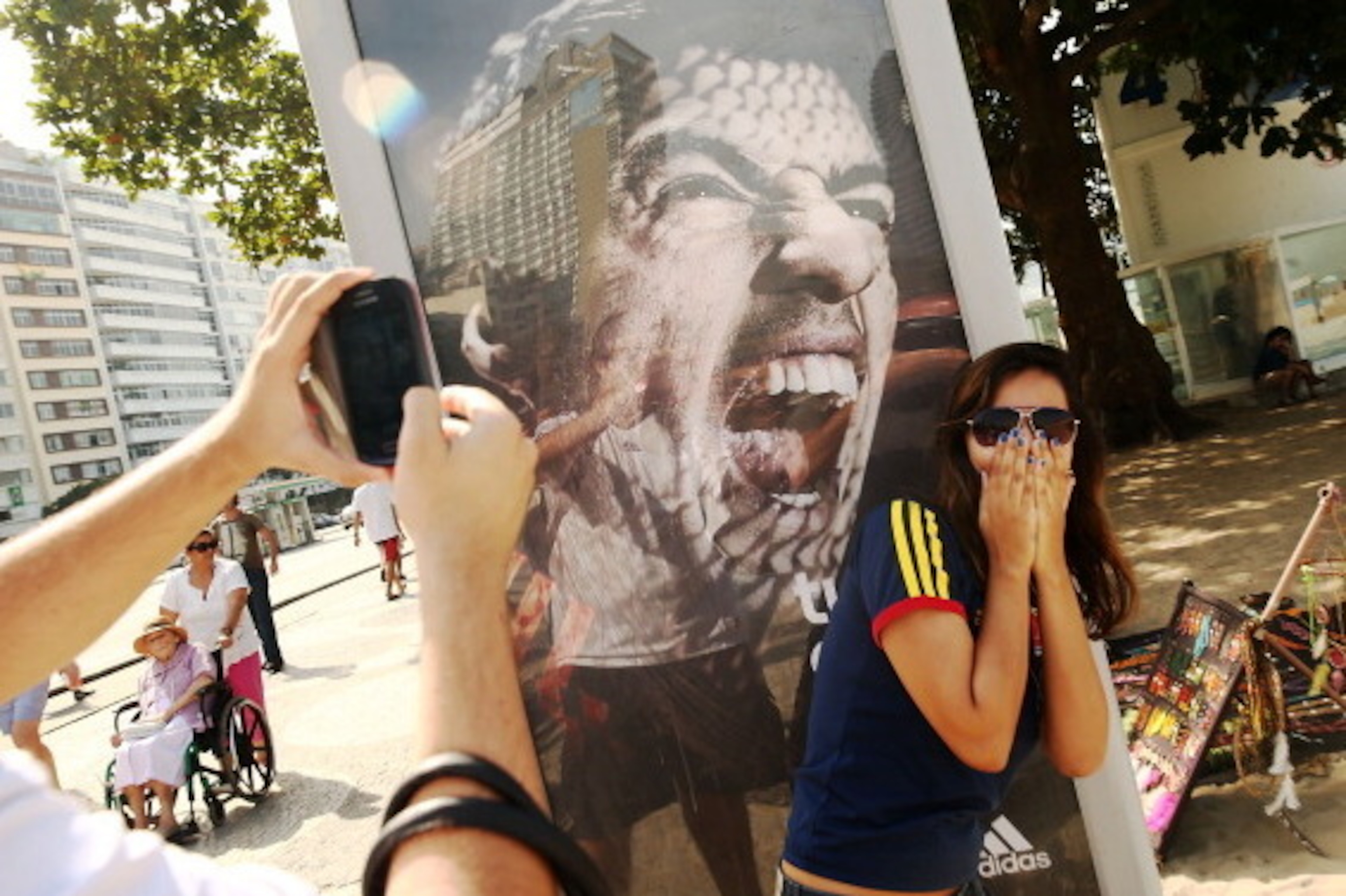 RIO DE JANEIRO, BRAZIL - JUNE 26:  A woman takes a photo next to an advertisement featuring Uruguay's Luis Suarez, mocking the biting incident against opponent Giorgio Chiellini during the World Cup match against Italy, on Copacabana Beach on June 26, 201