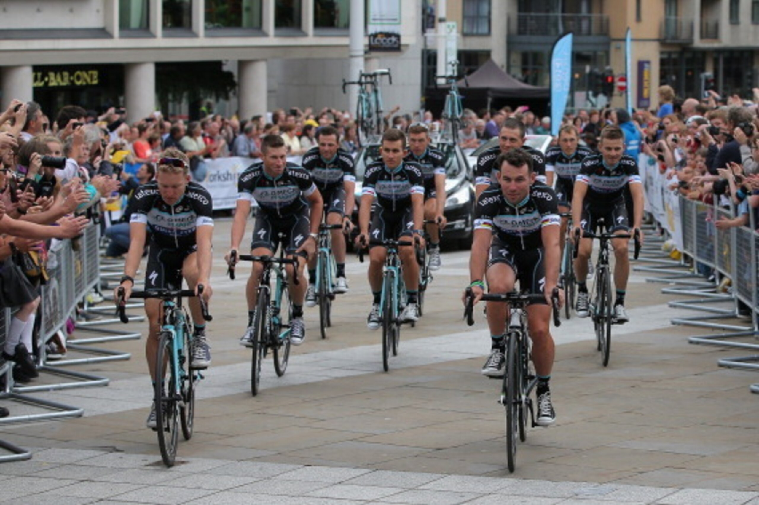 LEEDS, ENGLAND - JULY 03:  Mark Cavendish (R) of Great Britain riding for Omega Pharma/Quick-Step and his teammates are greeted by supporters as they ride through Millenium Square enroute to the Team Presentation prior to the 2014 Le Tour de France on Jul